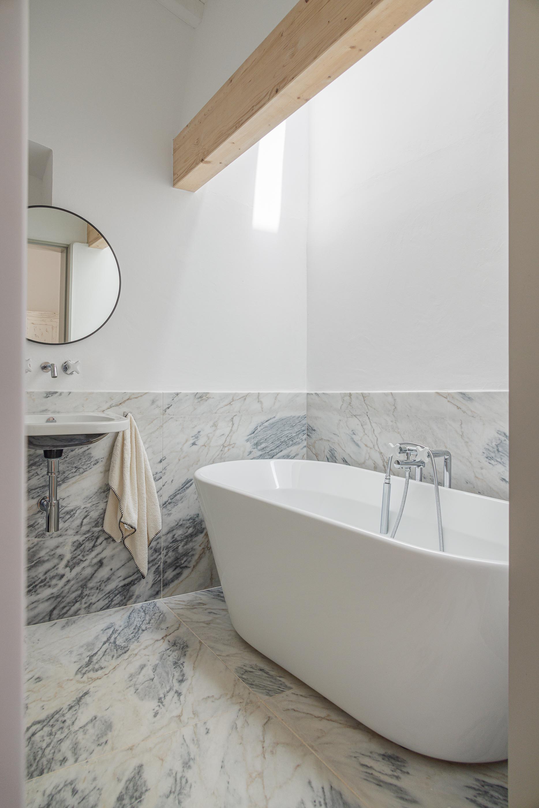 Casa de banho: Banheira branca, lavatório suspenso e revestimento em mármore. — Monte do Divor arquitetura Vasco Burnay Arquitectura em Estremoz