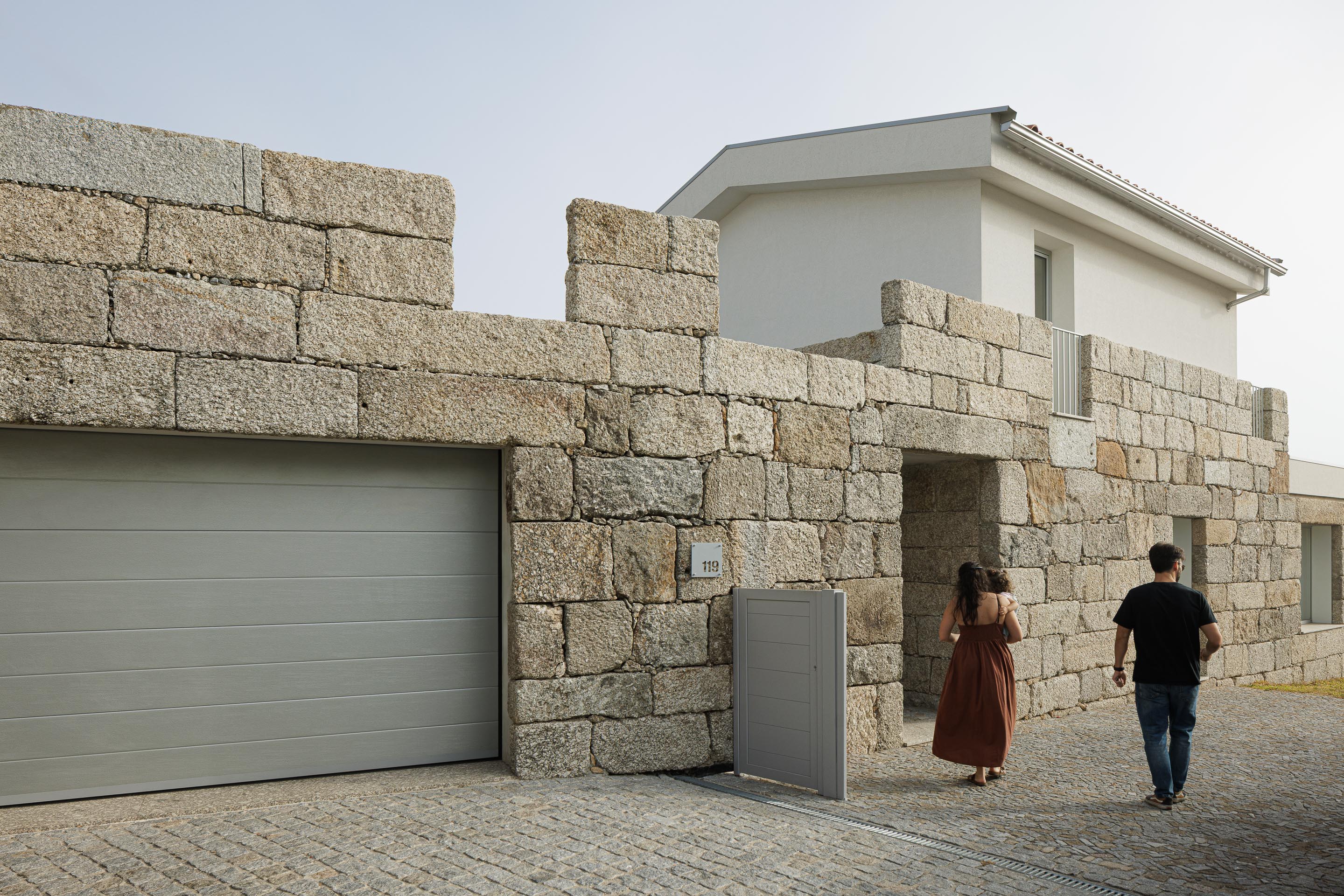 Entrada: Fachada em granito rústico com portão cinzento e garagem, integrando-se na paisagem. — Casa em Mesão Frio arquitetura felixARQS – Daniel Félix Arquitectos em Guimarães