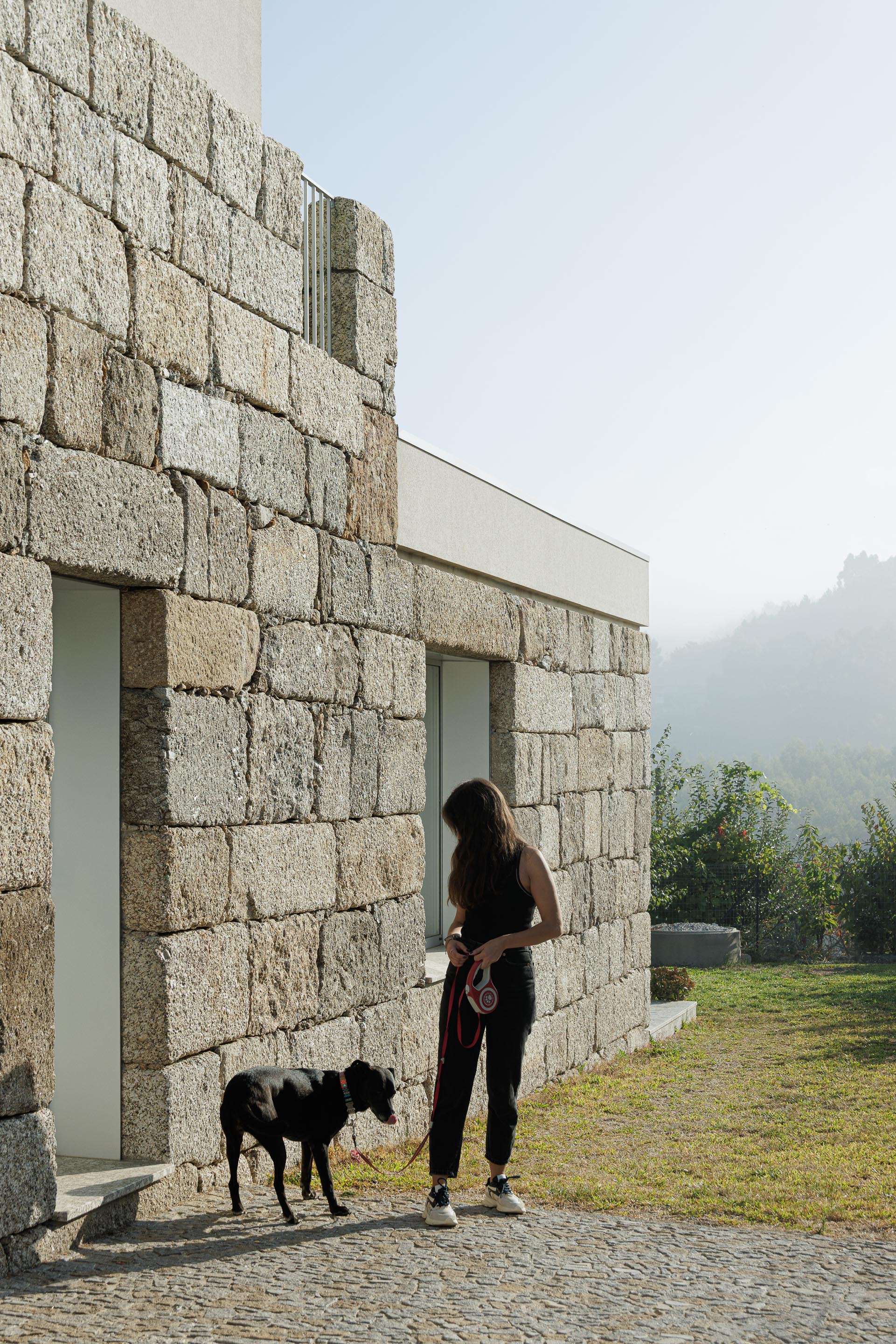 Exterior: Fachada em granito com janela minimalista, jardim relvado e vista para a serra. — Casa em Mesão Frio arquitetura felixARQS – Daniel Félix Arquitectos em Guimarães