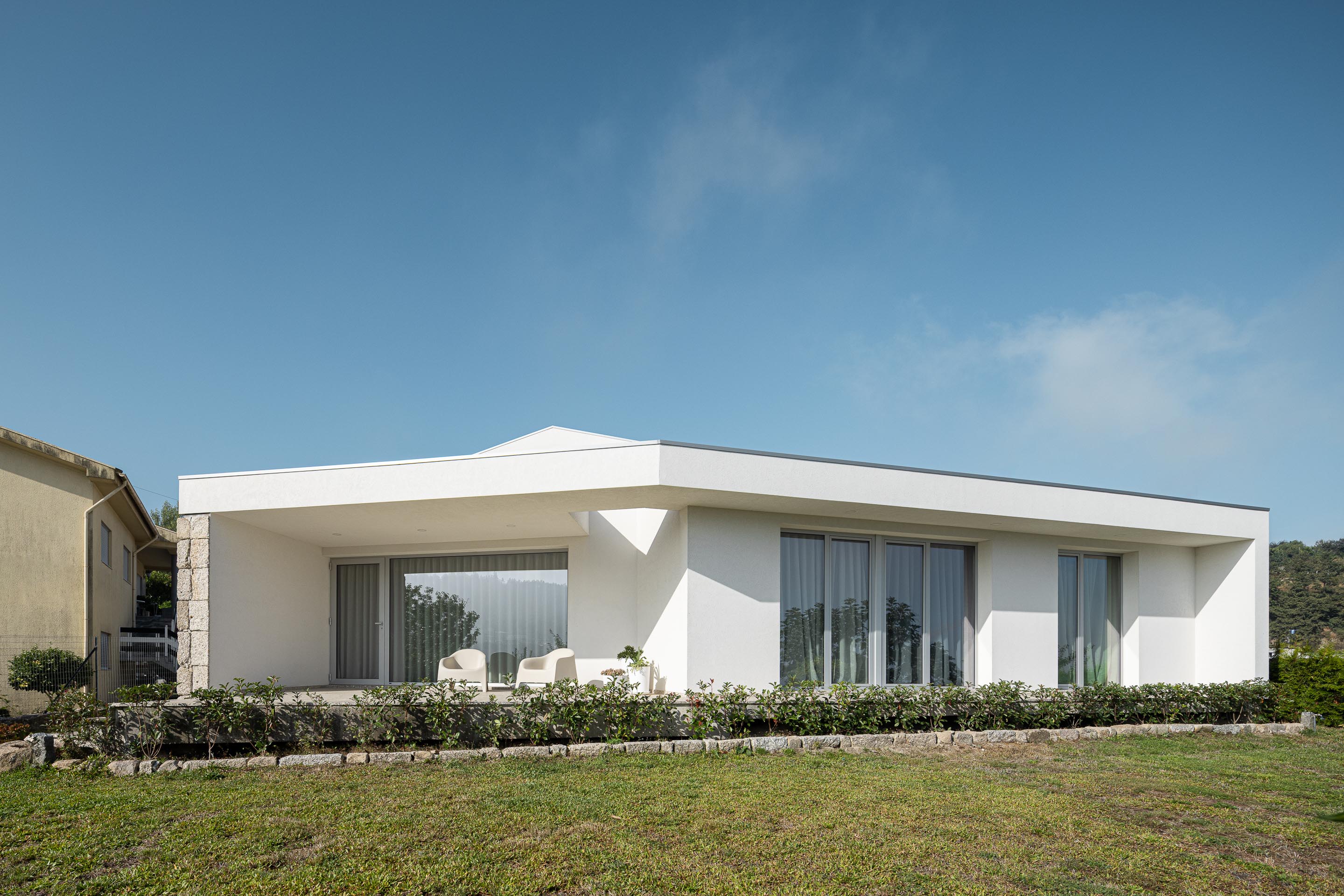 Exterior: Fachada minimalista branca com alpendre, cadeiras de exterior e jardim relvado. — Casa em Mesão Frio arquitetura felixARQS – Daniel Félix Arquitectos em Guimarães