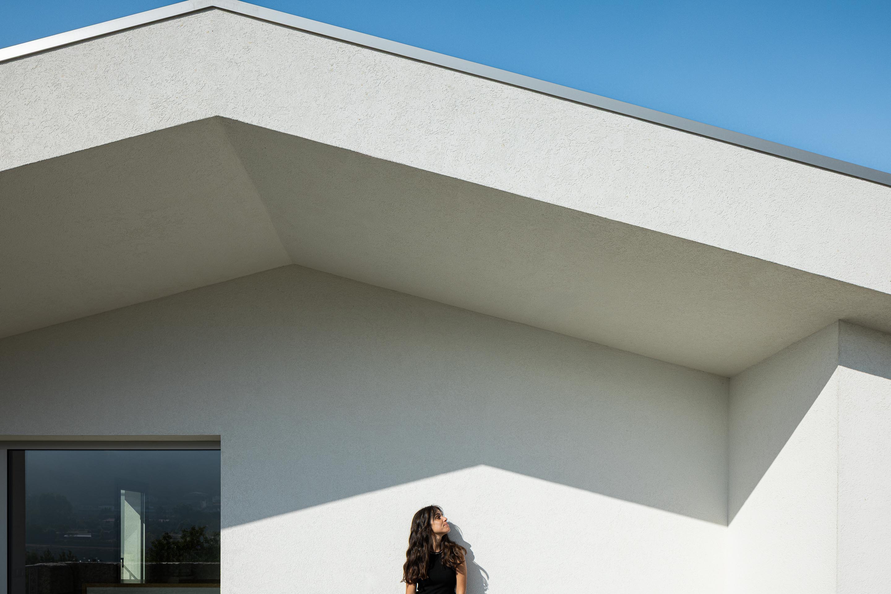 Exterior: Detalhe da fachada branca com janela e sombra, sob um céu azul. — Casa em Mesão Frio arquitetura felixARQS – Daniel Félix Arquitectos em Guimarães