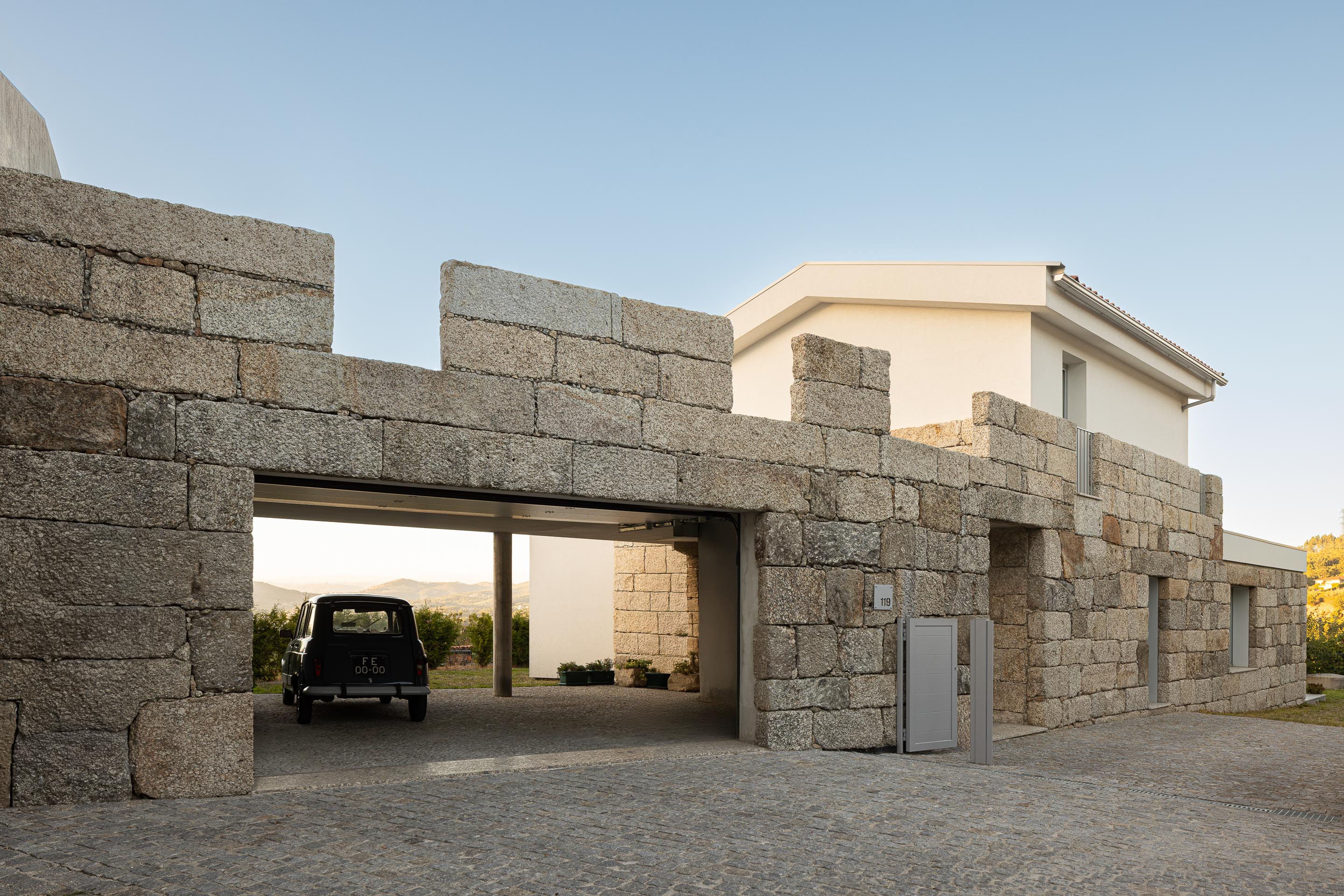 Exterior: Detalhe da garagem com carro clássico, sob uma estrutura de betão e granito. — Casa em Mesão Frio arquitetura felixARQS – Daniel Félix Arquitectos em Guimarães