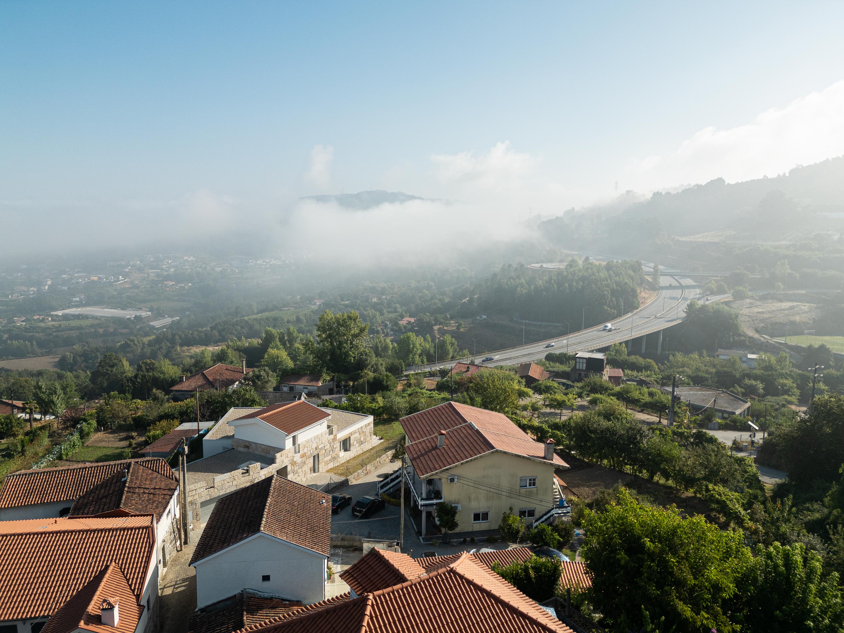 Exterior: Vista aérea da casa integrada na paisagem rural, com telhado de duas águas e alpendre. — Casa em Mesão Frio arquitetura felixARQS – Daniel Félix Arquitectos em Guimarães