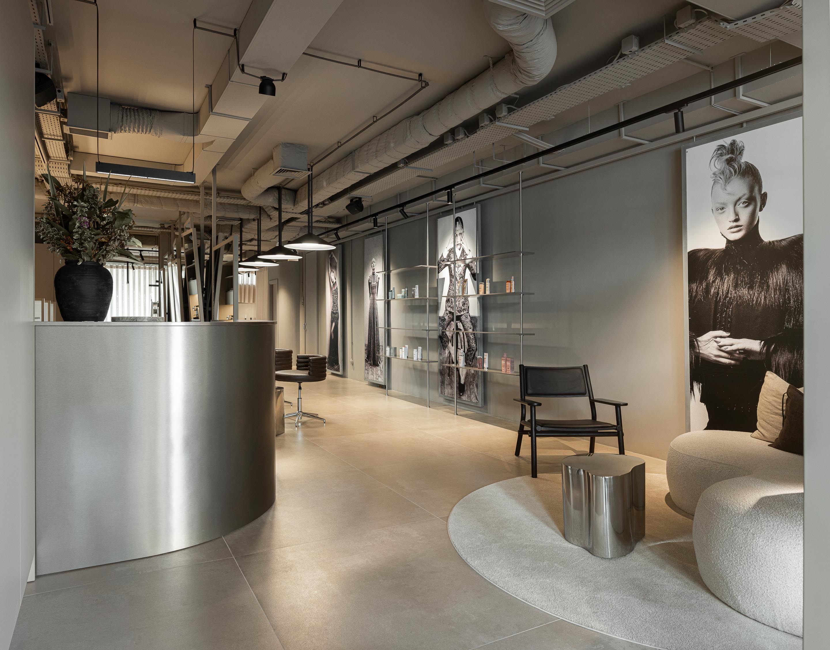 Recepção: Balcão curvo em metal, pavimento em tons neutros, iluminação industrial aparente e zona de espera com cadeirão. — Vasco Freitas Salon arquitetura MAT Arquitetura e Interiores em Porto