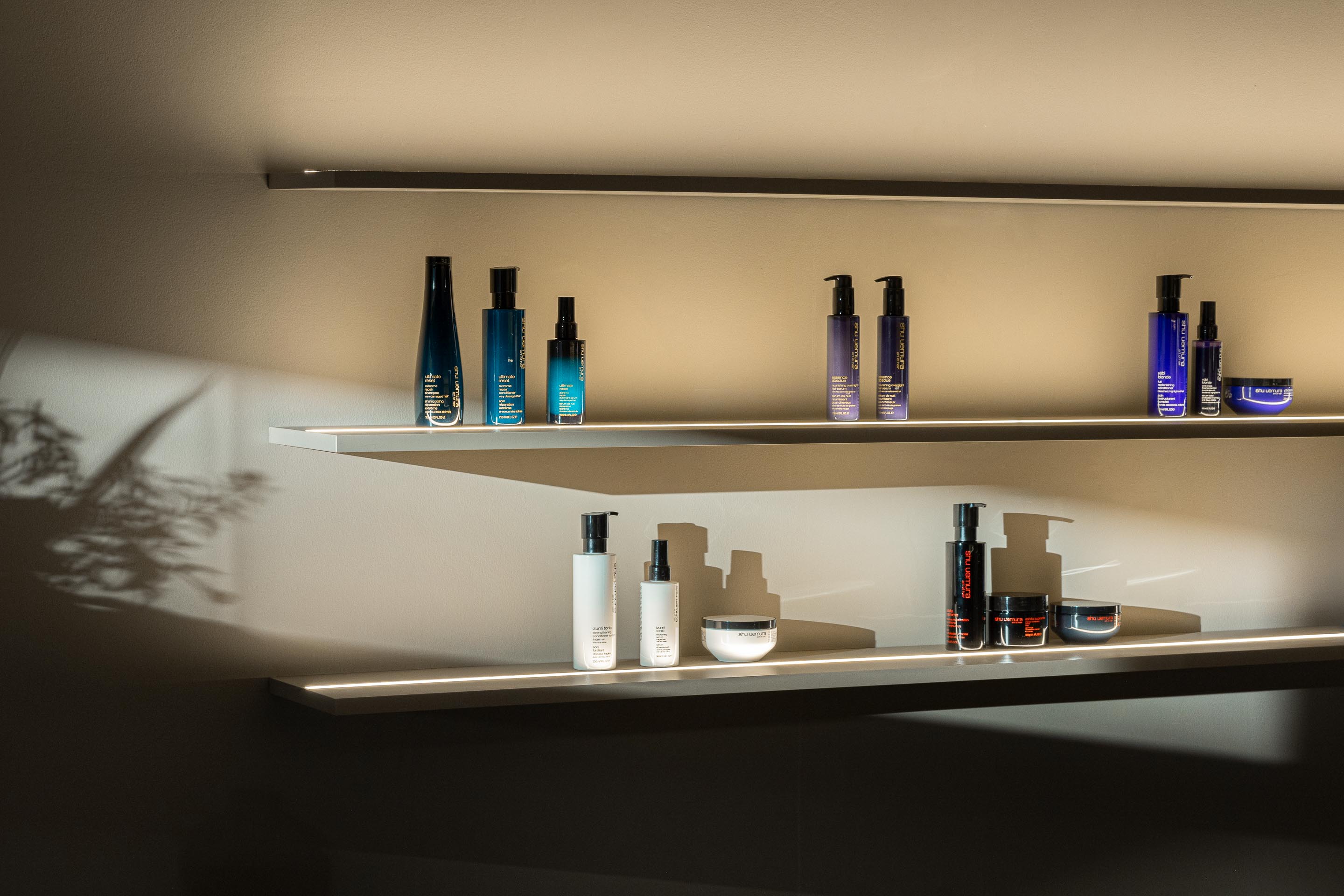 Detalhe: Prateleiras iluminadas com produtos de cabelo em embalagens variadas. — Vasco Freitas Salon arquitetura MAT Arquitetura e Interiores em Porto