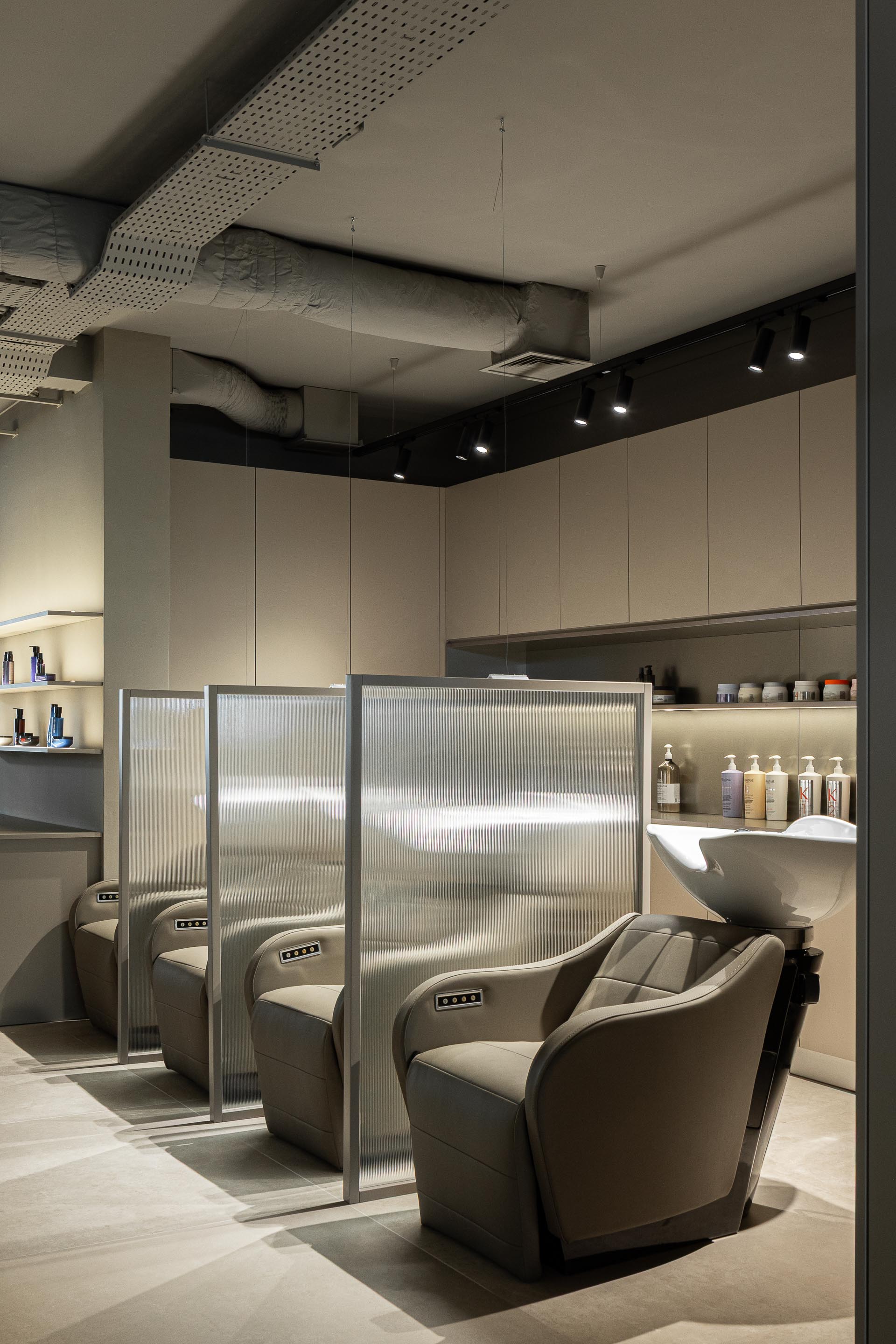 Lavagem: Cadeiras reclináveis para lavagem de cabelo, separadas por divisórias em vidro canelado. — Vasco Freitas Salon arquitetura MAT Arquitetura e Interiores em Porto