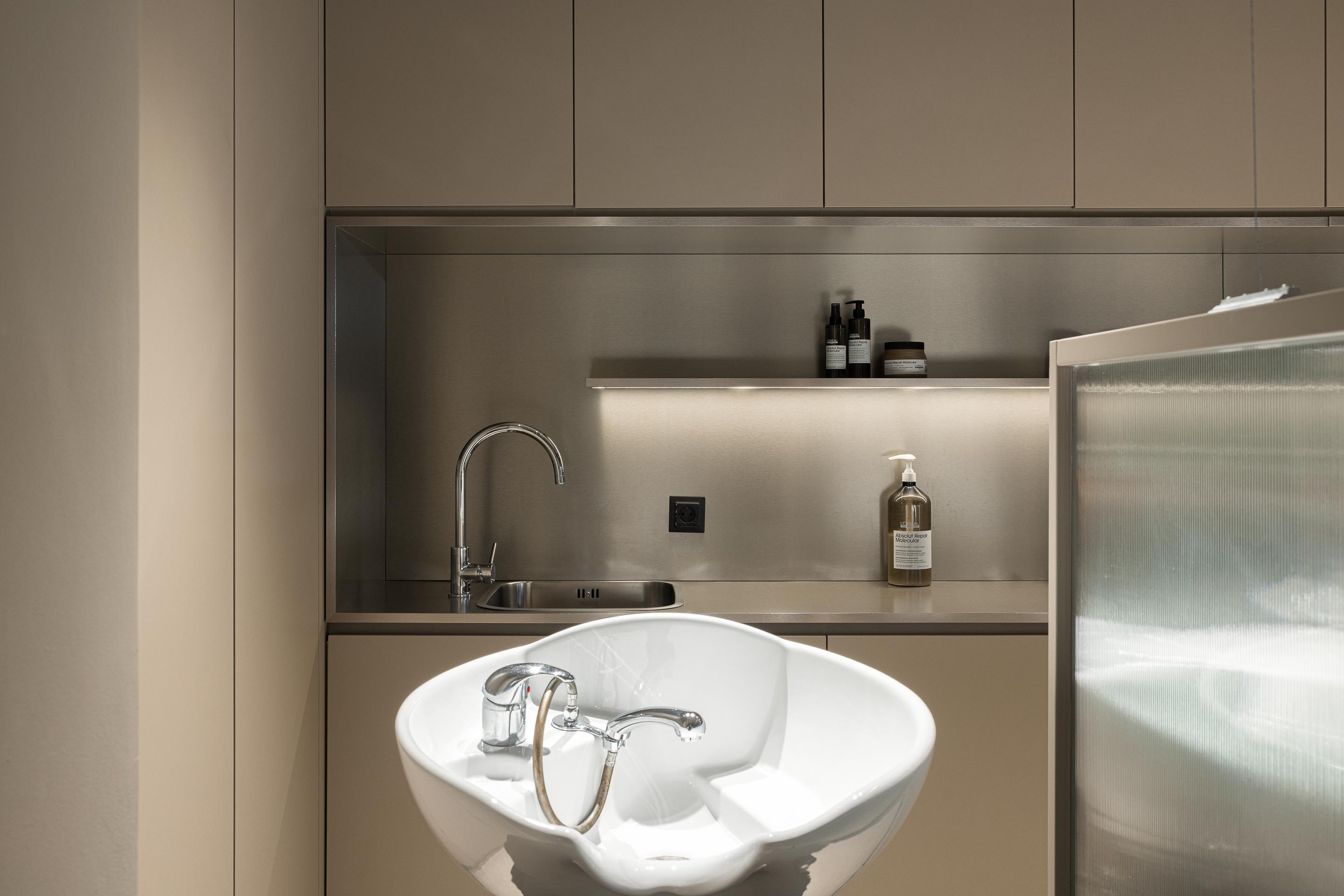 Lavagem: Detalhe do lavatório com torneira cromada e produtos de cabelo. — Vasco Freitas Salon arquitetura MAT Arquitetura e Interiores em Porto