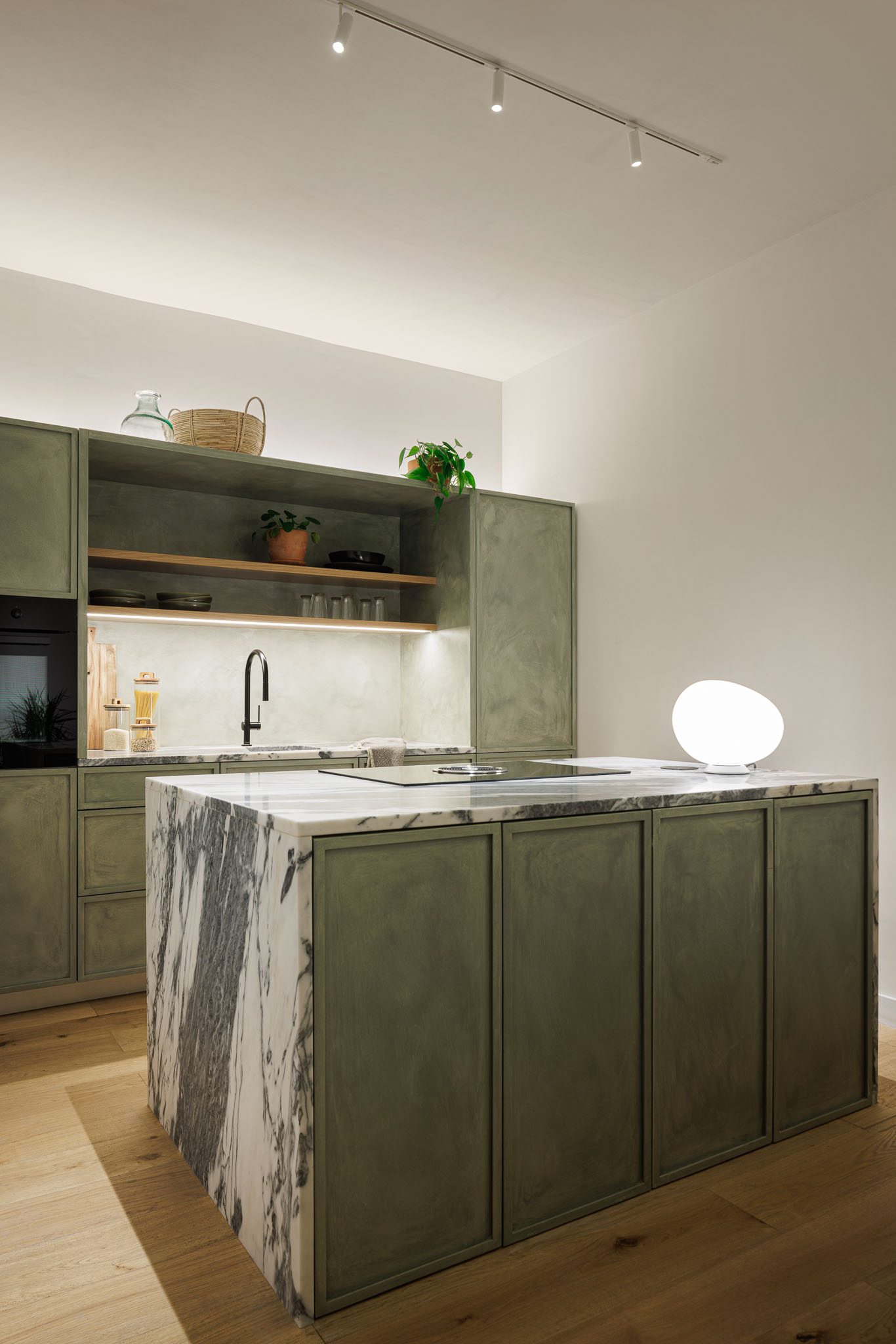 Cozinha: Ilha central com bancada em mármore e armários verdes, pavimento em madeira clara. — Urban Retreat arquitetura Atelier Réalité em Lisboa