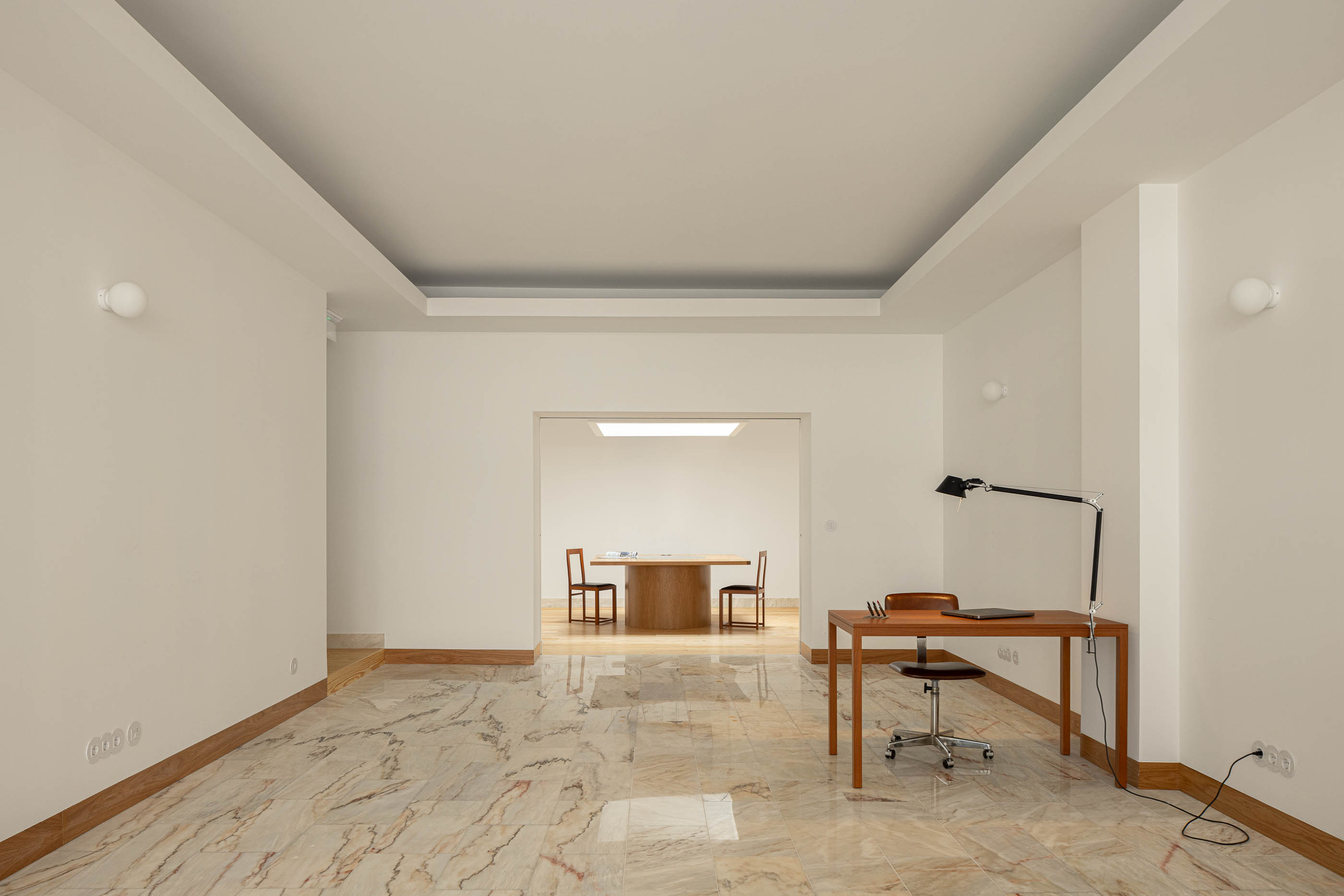 Escritório com pavimento em mármore, paredes brancas, candeeiros de parede e secretária de madeira com cadeira giratória. — Reconversão do Talho Central arquitetura José Pedro Lima Arquiteto em Coimbra