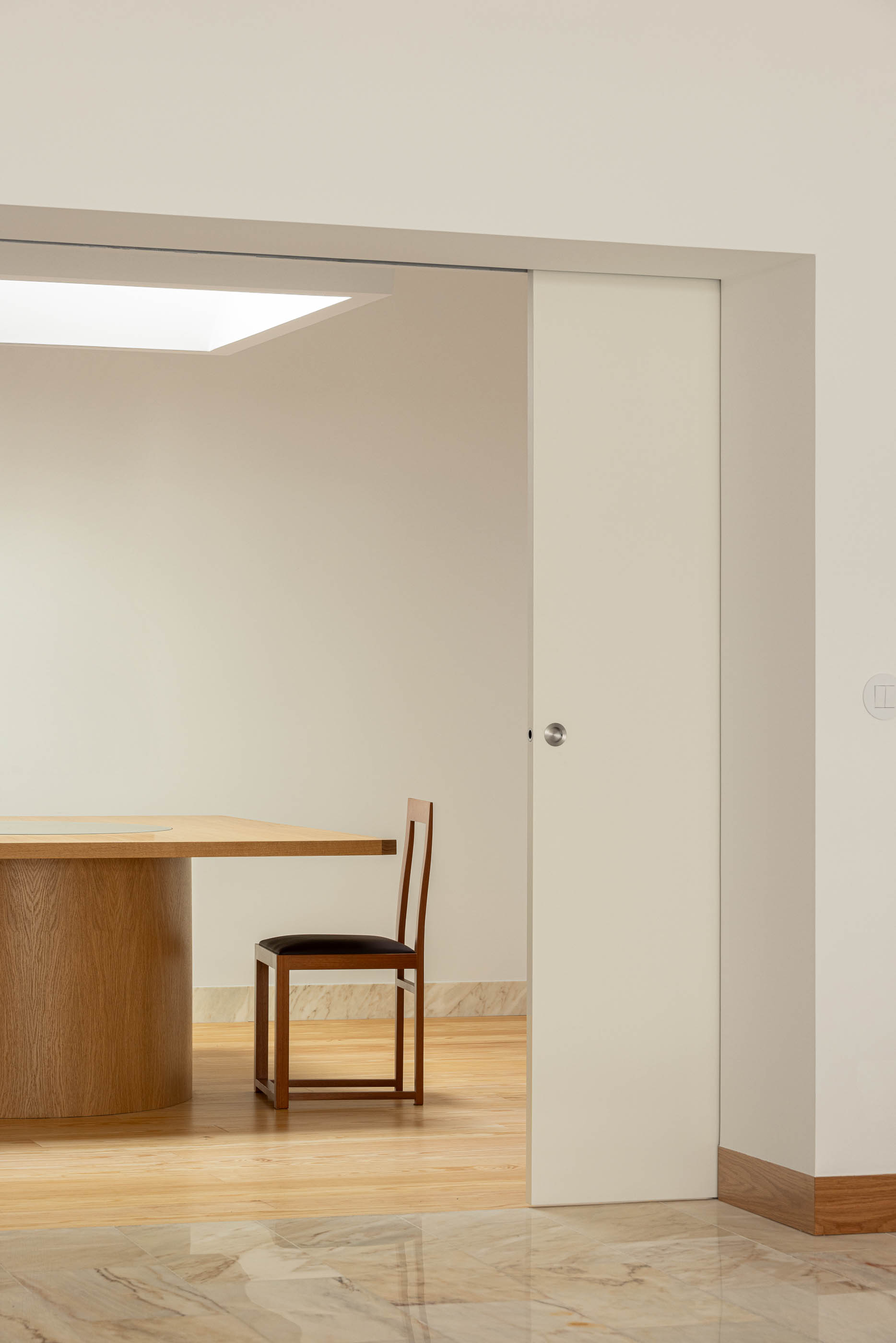 Escritório com pavimento em mármore e porta de correr aberta para sala de reuniões. Cadeira de madeira junto à mesa. — Reconversão do Talho Central arquitetura José Pedro Lima Arquiteto em Coimbra