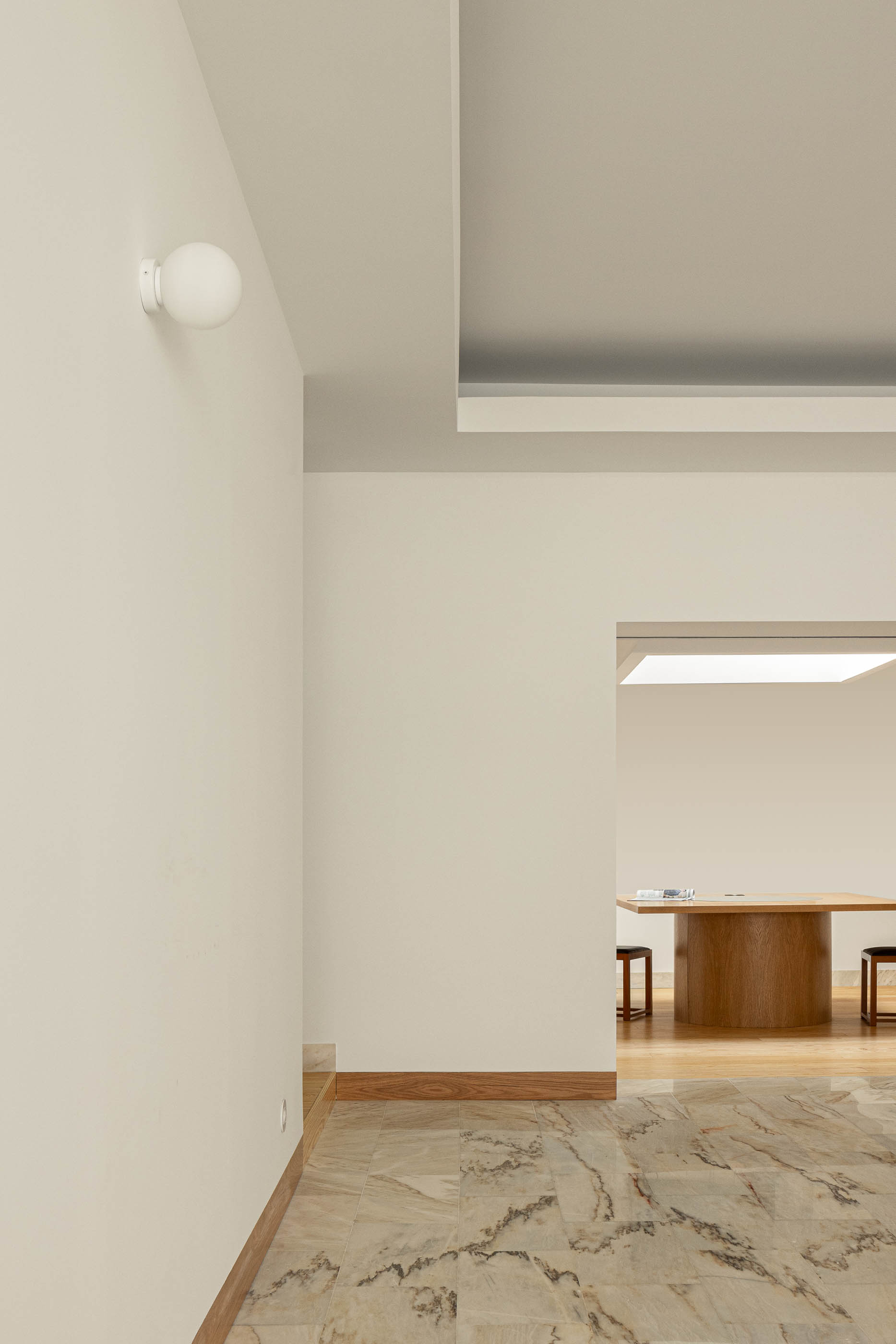 Escritório com pavimento em mármore, candeeiro de parede e porta de acesso à sala de reuniões com mesa redonda. — Reconversão do Talho Central arquitetura José Pedro Lima Arquiteto em Coimbra