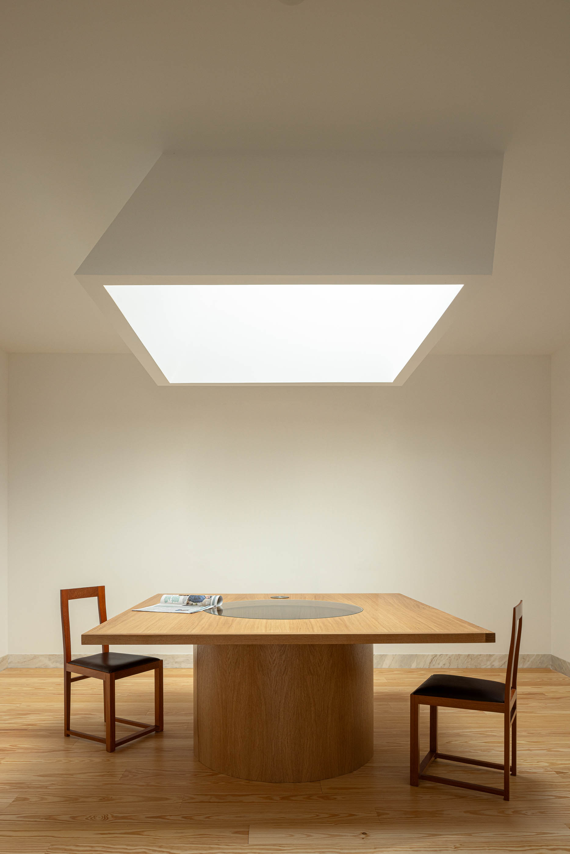 Sala de reuniões com mesa redonda em madeira e cadeiras. Pavimento em madeira e iluminação zenital. — Reconversão do Talho Central arquitetura José Pedro Lima Arquiteto em Coimbra