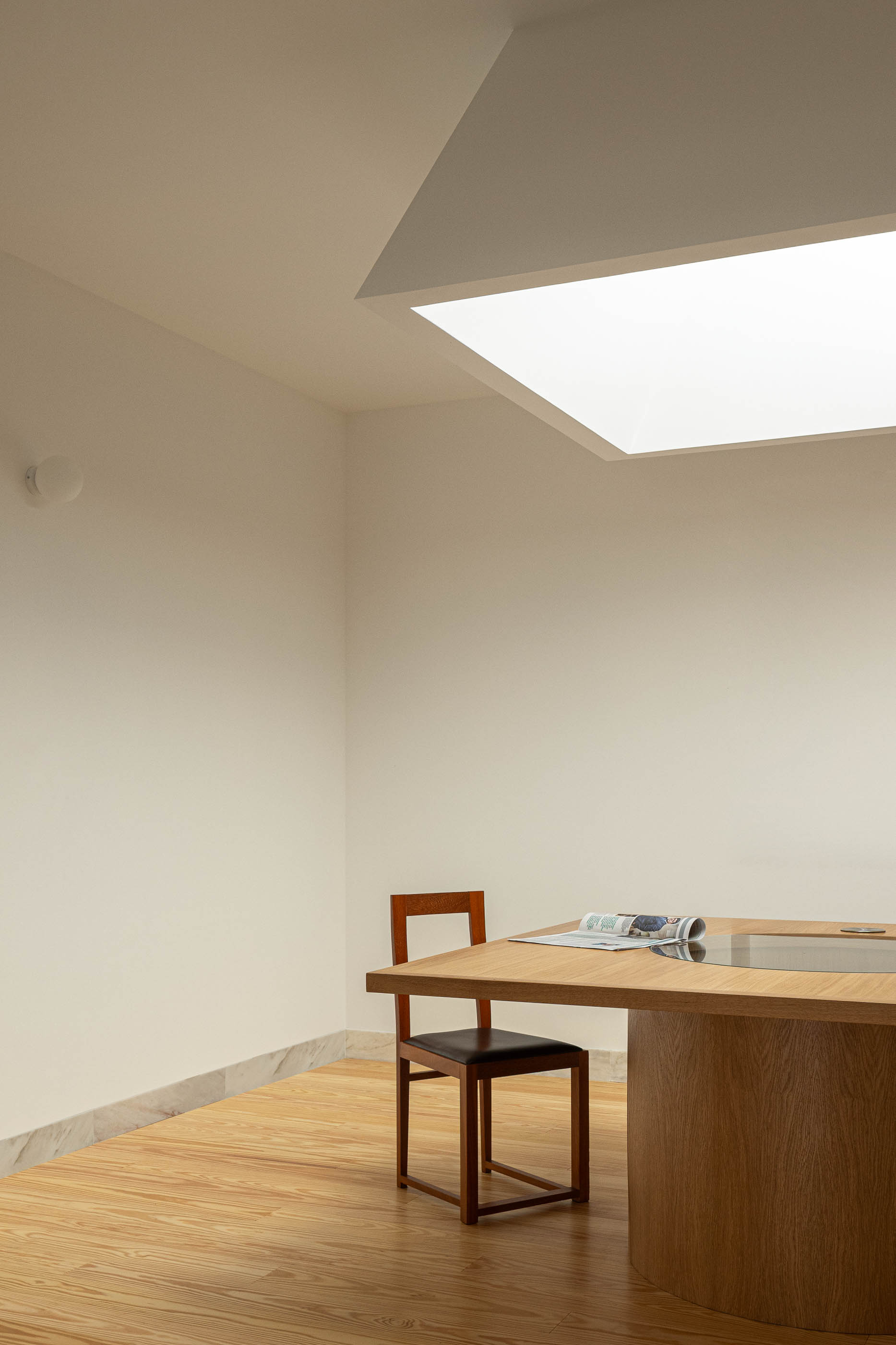 Sala de reuniões com mesa redonda em madeira e cadeiras. Pavimento em madeira e iluminação zenital. — Reconversão do Talho Central arquitetura José Pedro Lima Arquiteto em Coimbra