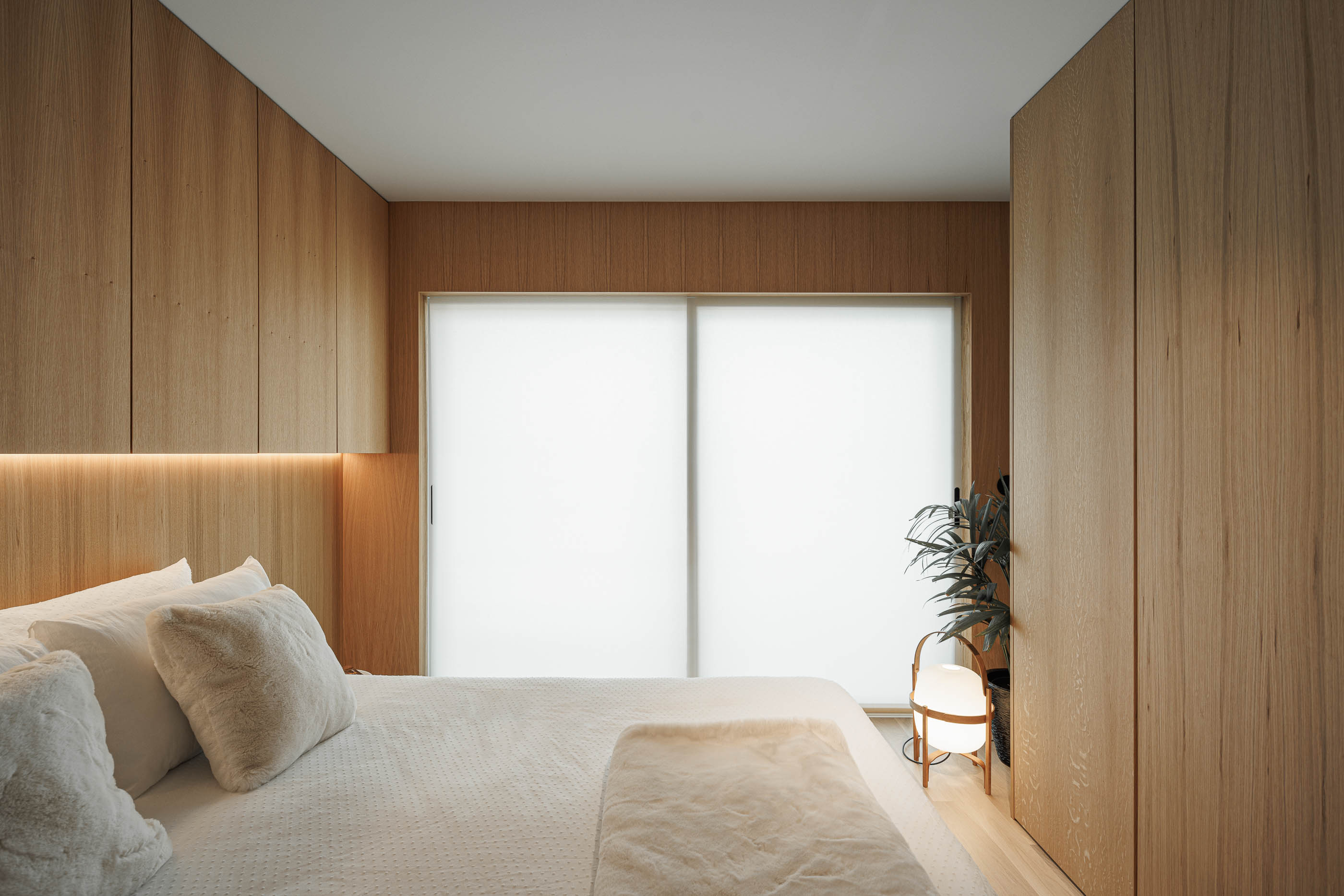 Quarto: Cama de casal com cabeceira e armários em madeira clara, candeeiro de pé moderno e cortinas translúcidas. — Barra Apartment arquitetura Paulo Martins Arquitectura e Design em Aveiro