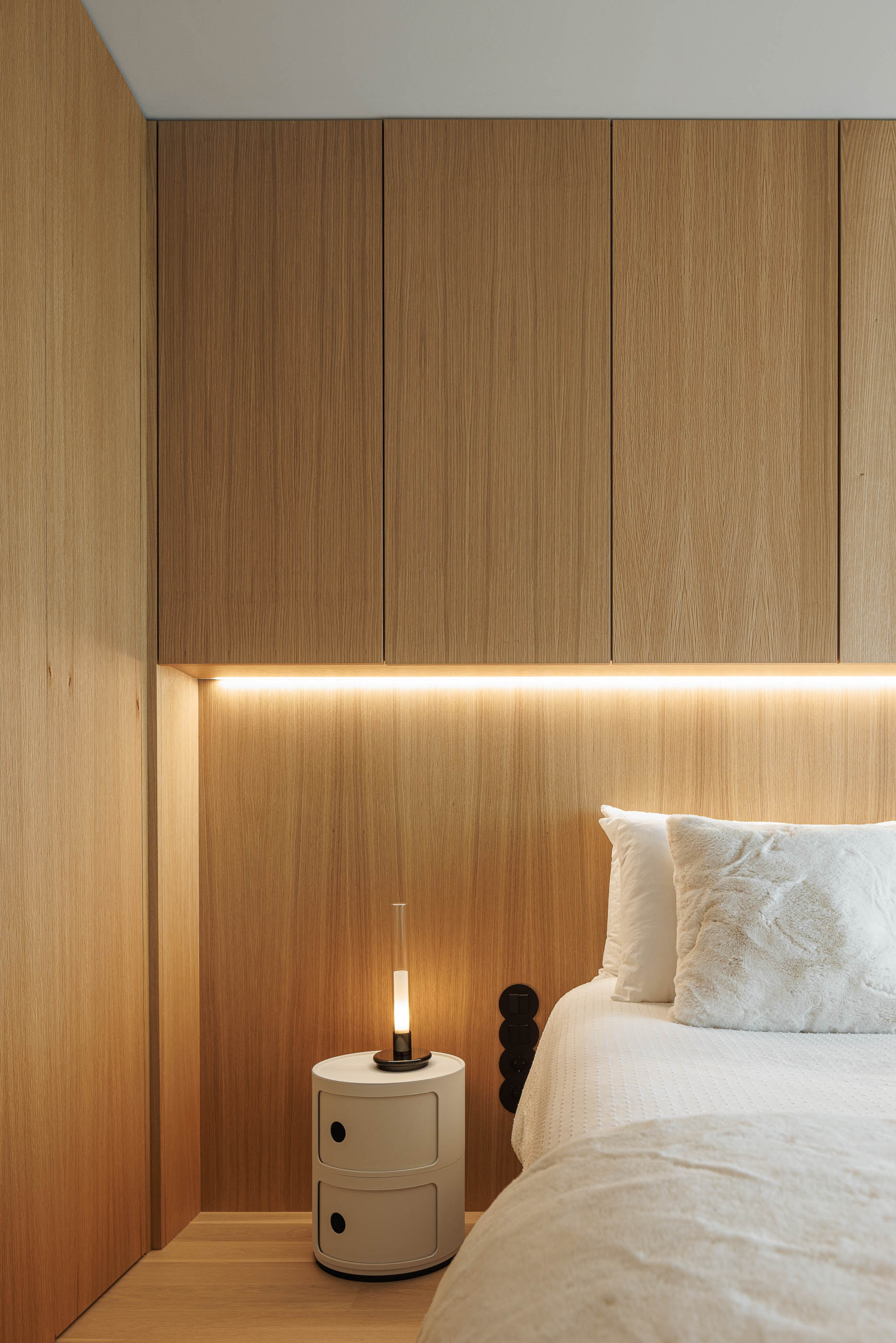 Quarto: Detalhe da cabeceira em madeira com iluminação embutida, mesa de cabeceira redonda e candeeiro minimalista. — Barra Apartment arquitetura Paulo Martins Arquitectura e Design em Aveiro