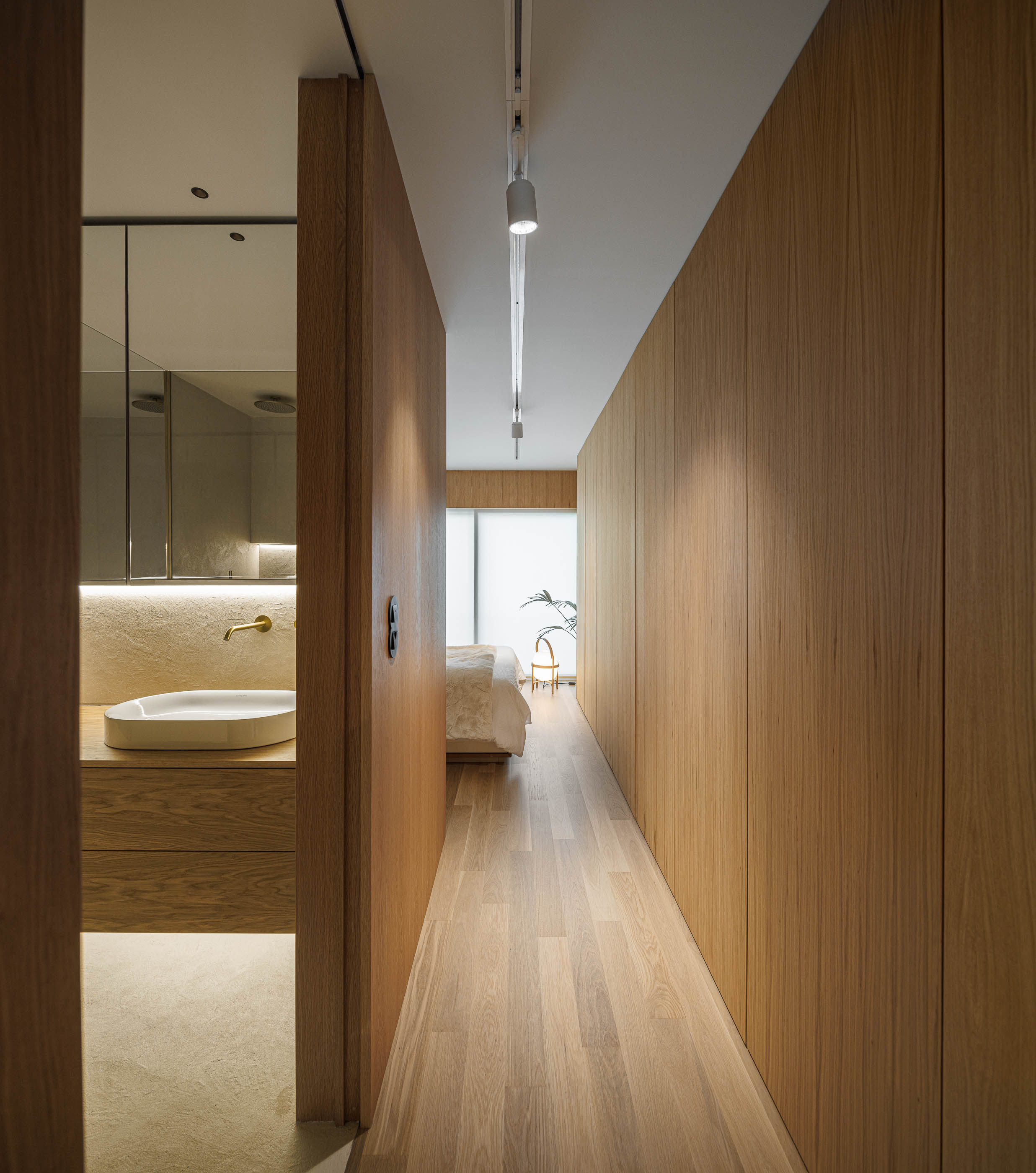 Corredor: Perspectiva do corredor com armários em madeira, pavimento em madeira clara e acesso à casa de banho e quarto. — Barra Apartment arquitetura Paulo Martins Arquitectura e Design em Aveiro