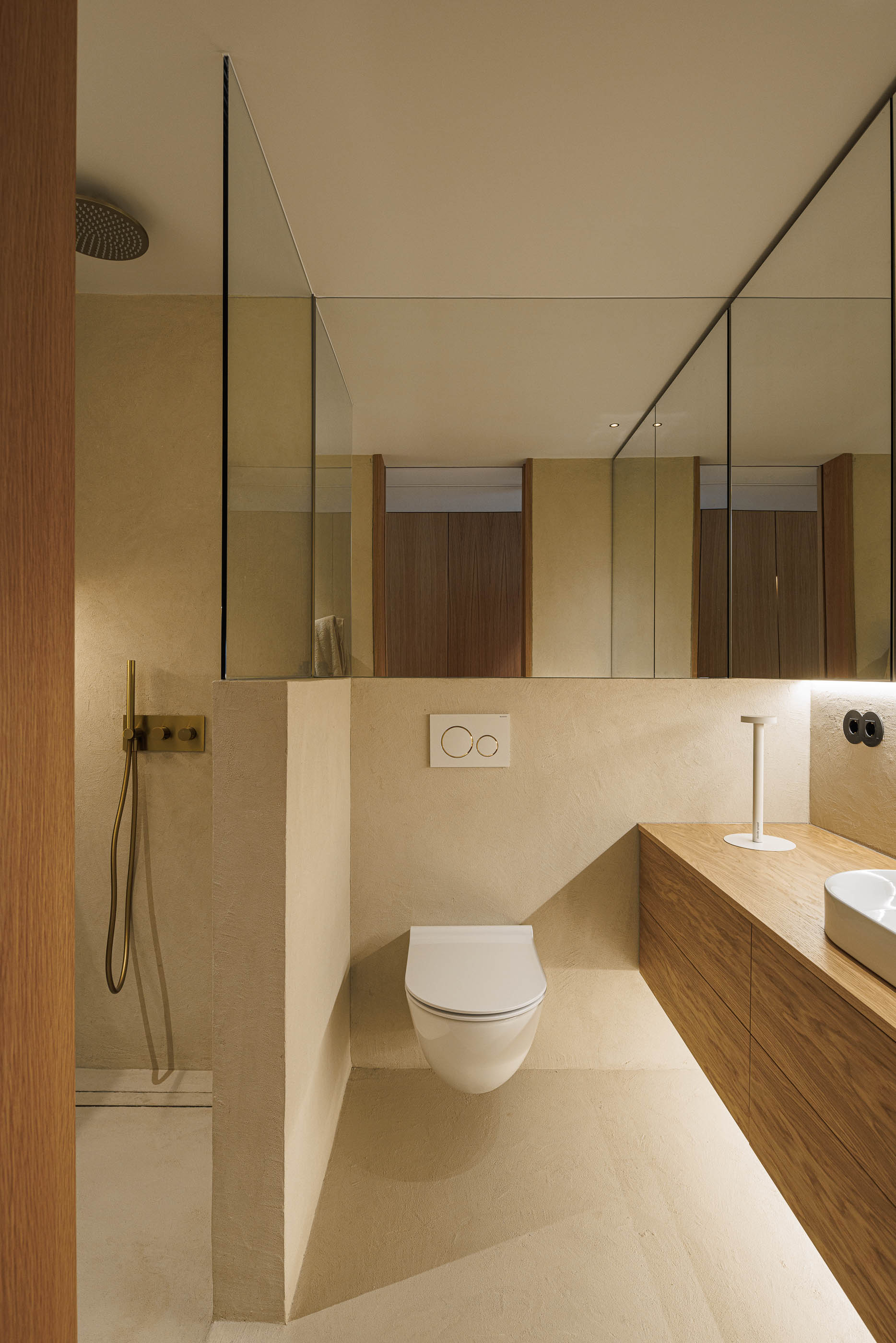 Casa de banho: Sanita suspensa, duche com resguardo em vidro e lavatório sobre móvel em madeira clara. — Barra Apartment arquitetura Paulo Martins Arquitectura e Design em Aveiro