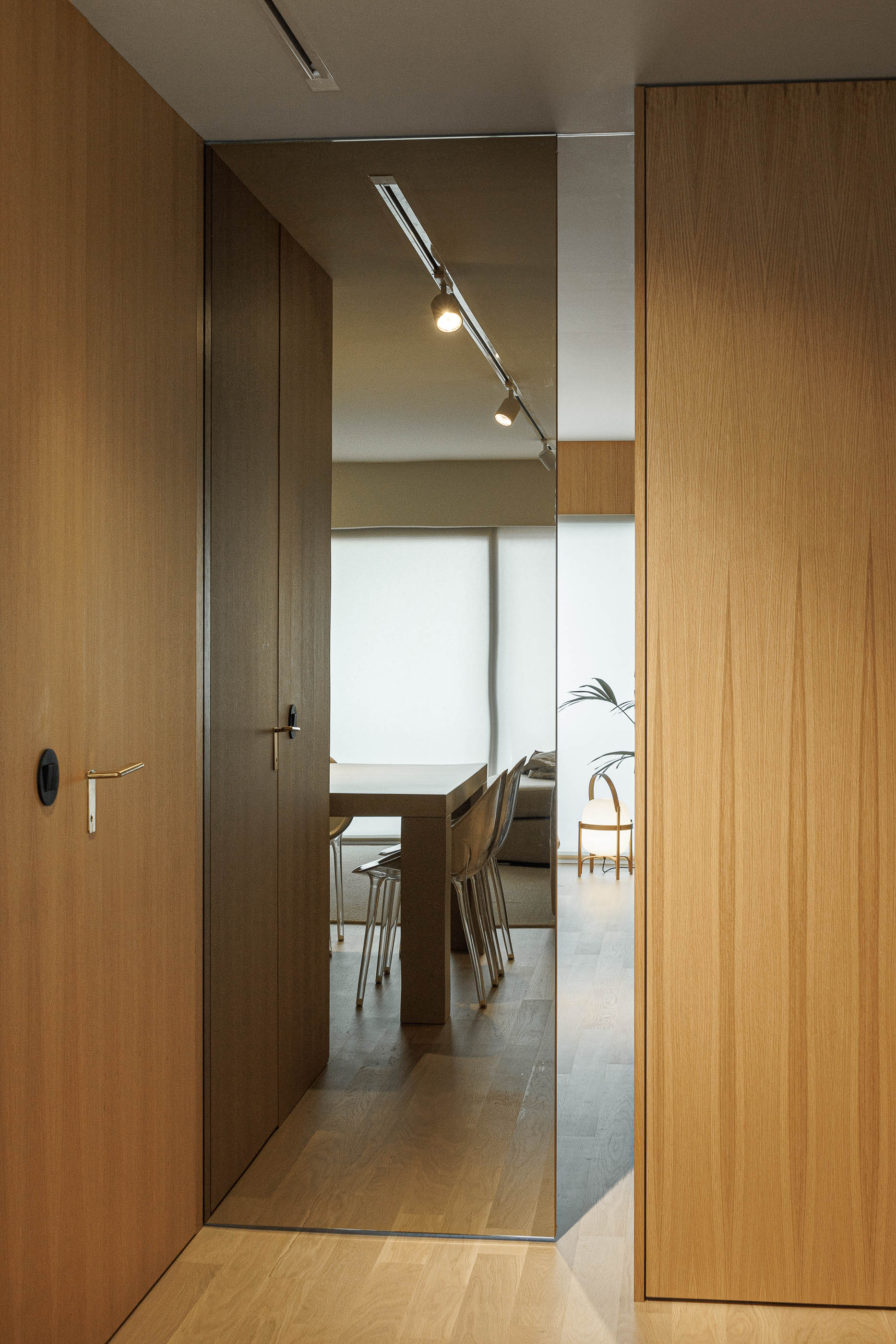 Sala de jantar: Vista da sala de jantar com mesa e cadeiras transparentes, através de uma porta espelhada no corredor. — Barra Apartment arquitetura Paulo Martins Arquitectura e Design em Aveiro