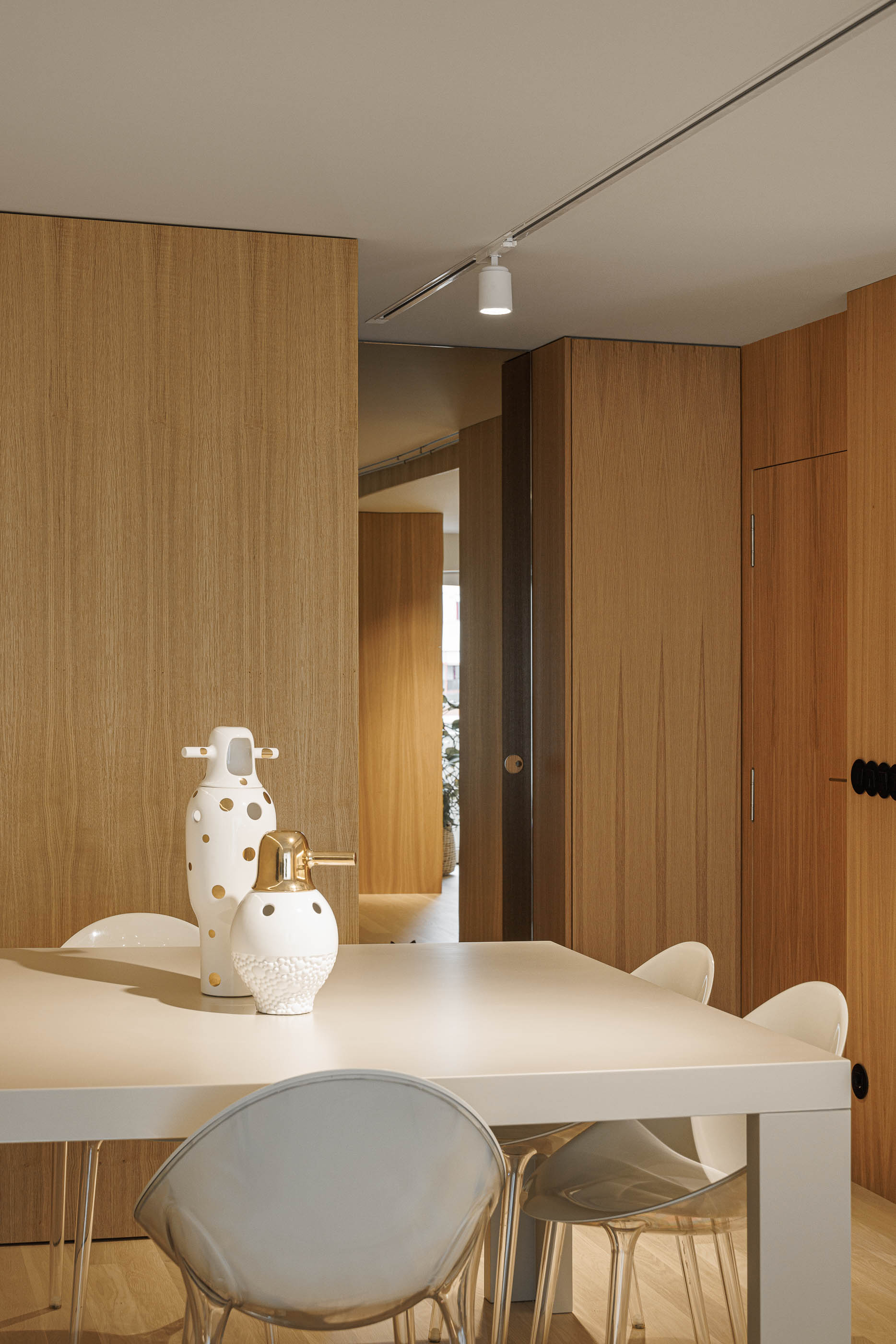 Sala de jantar: Mesa de jantar branca com cadeiras transparentes e objectos decorativos, com vista para o corredor. — Barra Apartment arquitetura Paulo Martins Arquitectura e Design em Aveiro
