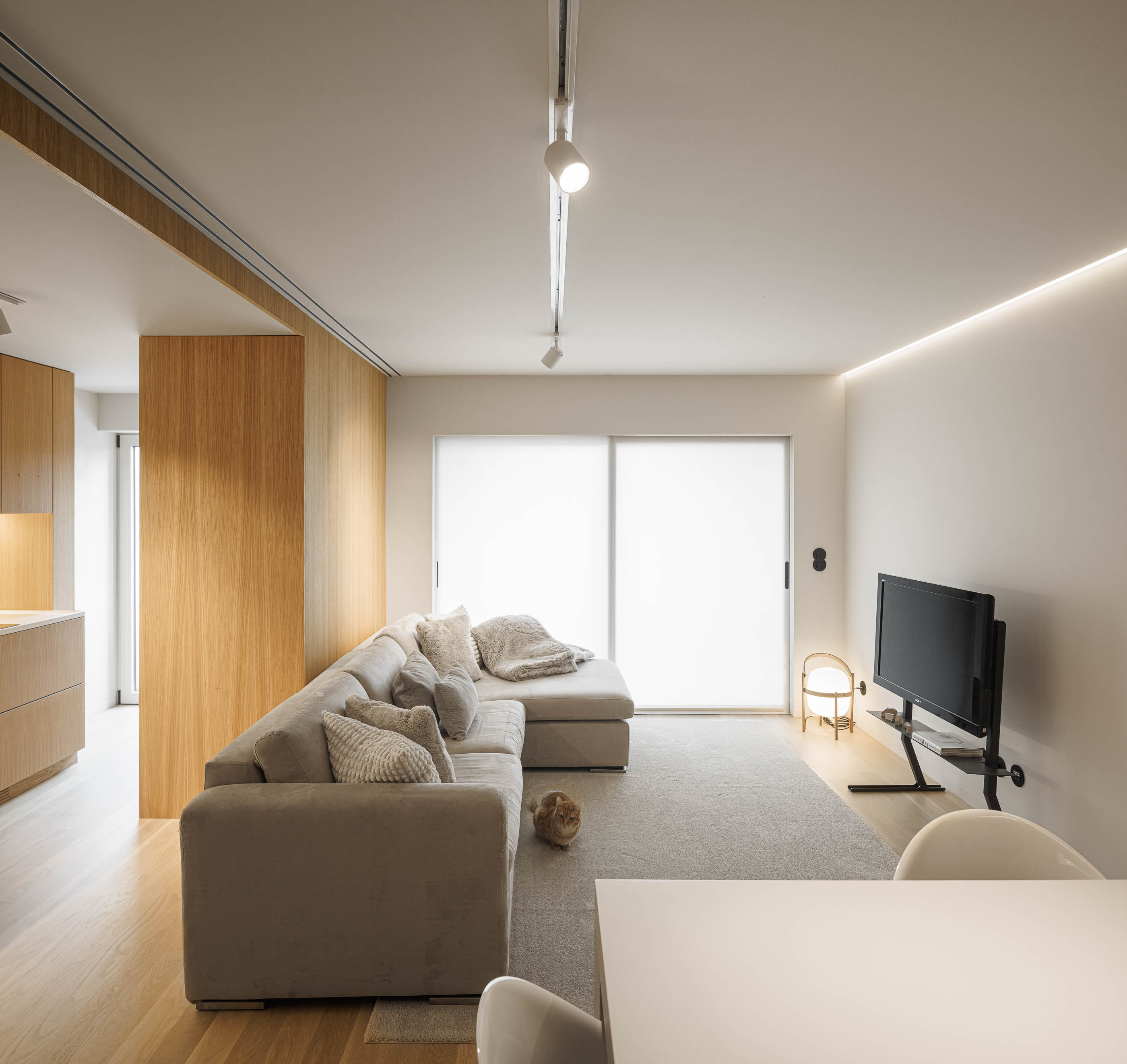 Sala de estar: Sofá bege com almofadas, televisão na parede, candeeiro de pé e alcatifa clara na sala de estar. — Barra Apartment arquitetura Paulo Martins Arquitectura e Design em Aveiro