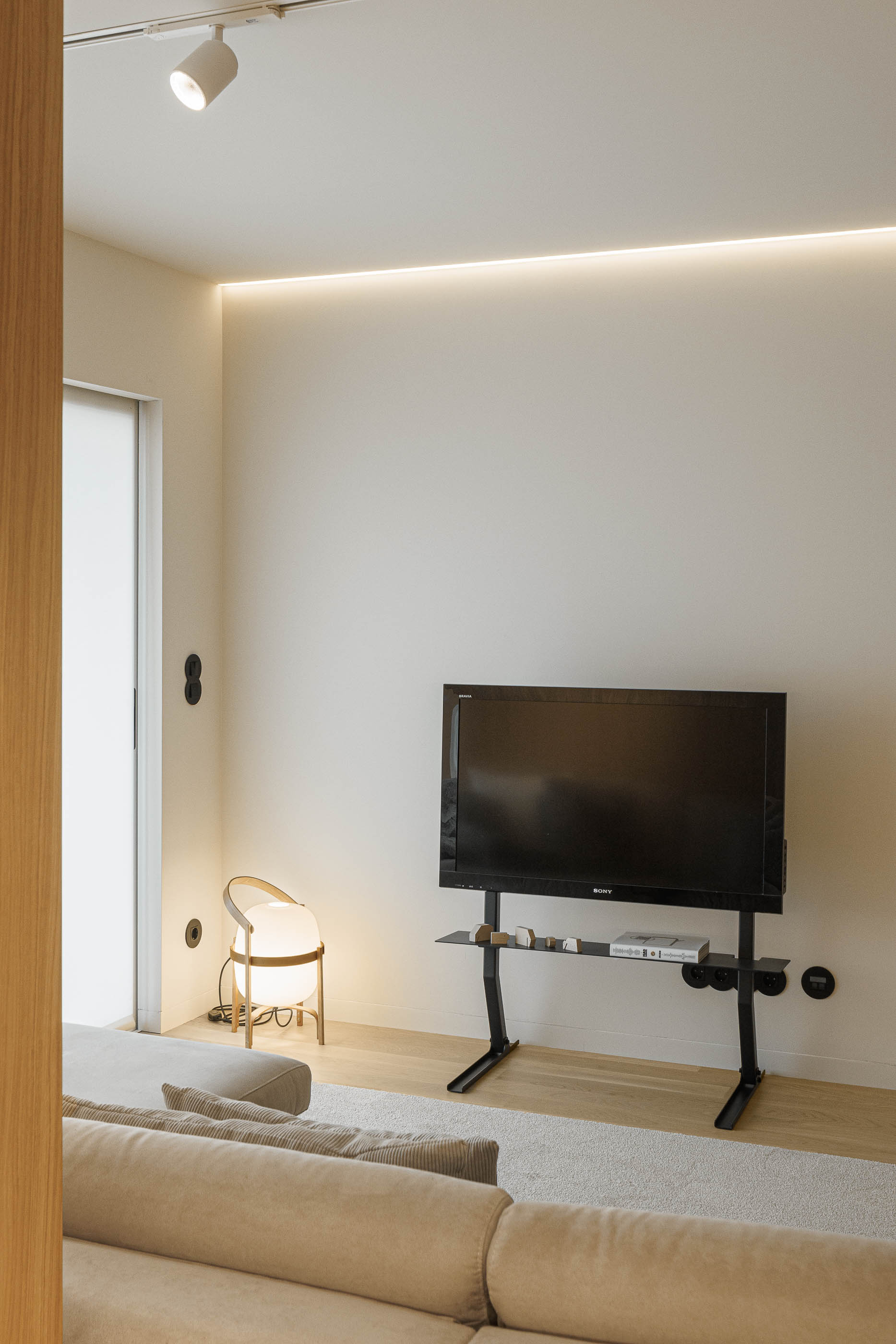 Sala de estar: Detalhe da televisão na parede, candeeiro de pé e alcatifa clara na sala de estar. — Barra Apartment arquitetura Paulo Martins Arquitectura e Design em Aveiro