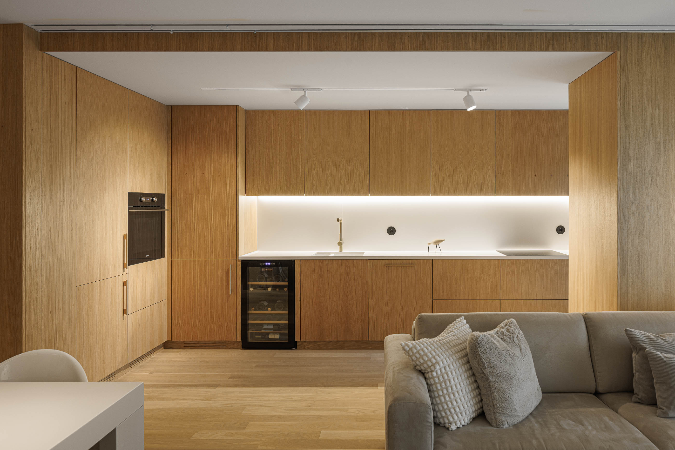 Cozinha: Cozinha em madeira clara com forno, garrafeira e iluminação embutida, integrada na sala de estar. — Barra Apartment arquitetura Paulo Martins Arquitectura e Design em Aveiro