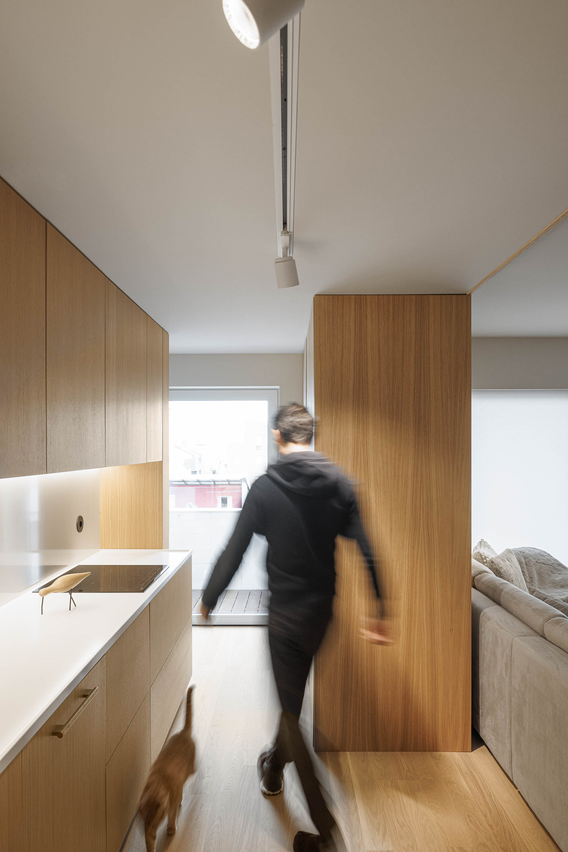 Cozinha: Cozinha em madeira clara com bancada branca, placa de fogão e acesso à varanda. — Barra Apartment arquitetura Paulo Martins Arquitectura e Design em Aveiro