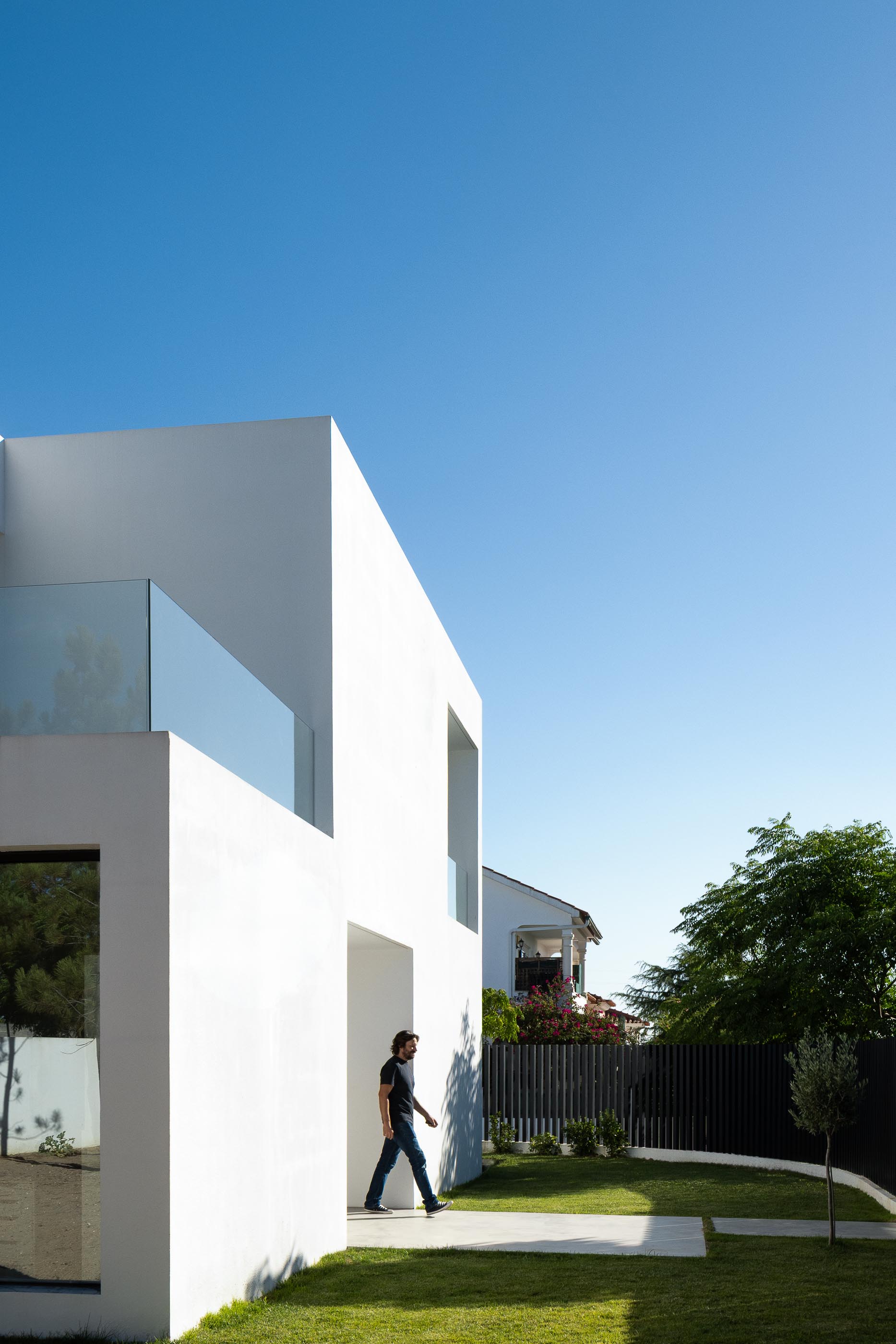 Exterior: Homem a caminhar no relvado junto à casa branca de arquitetura moderna. — Casa DR arquitetura NMDARQ – Nuno Miguel Dias, Arquitecto em Torres Novas