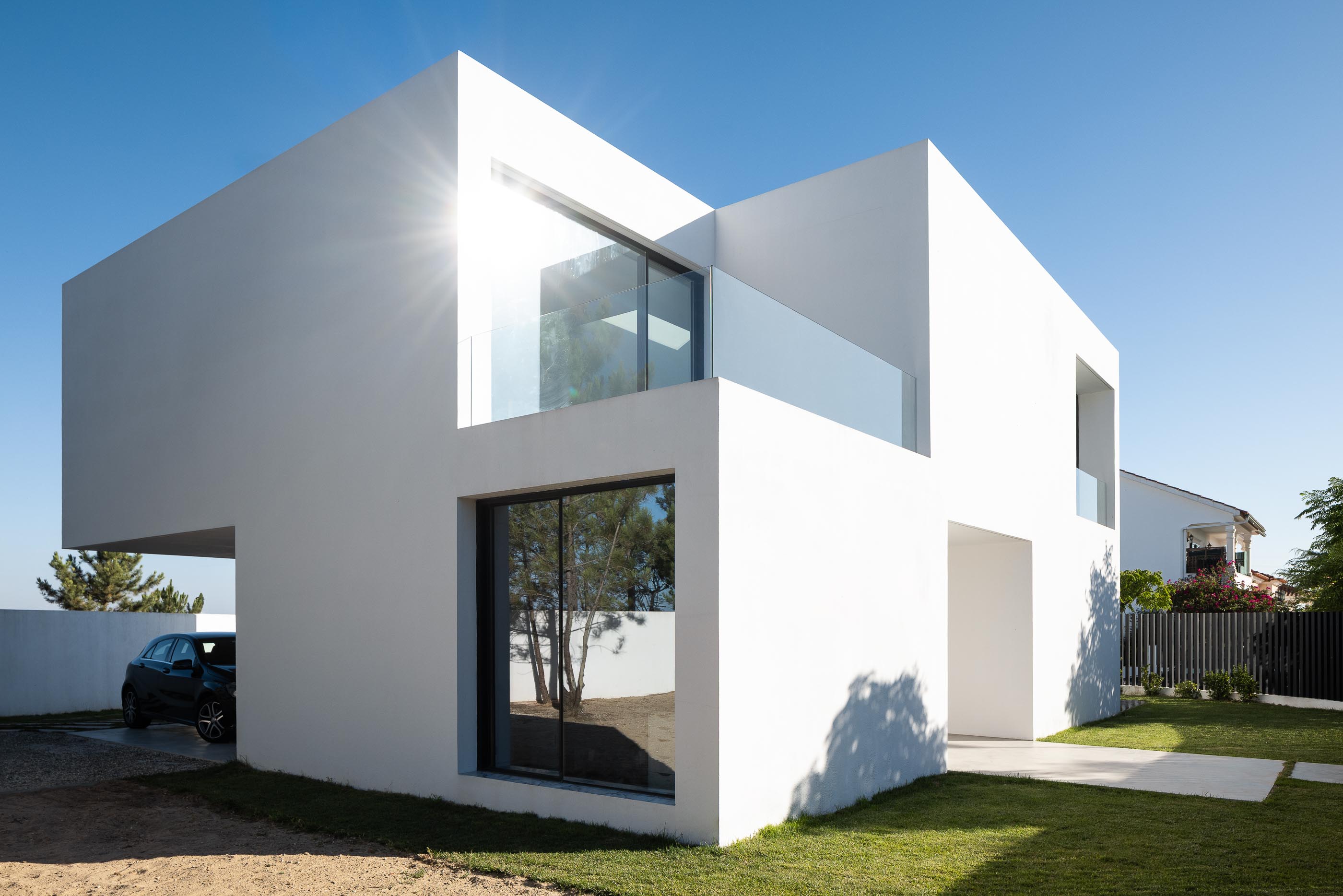 Exterior: Perspectiva da casa branca com garagem, relvado e janelas amplas. — Casa DR arquitetura NMDARQ – Nuno Miguel Dias, Arquitecto em Torres Novas