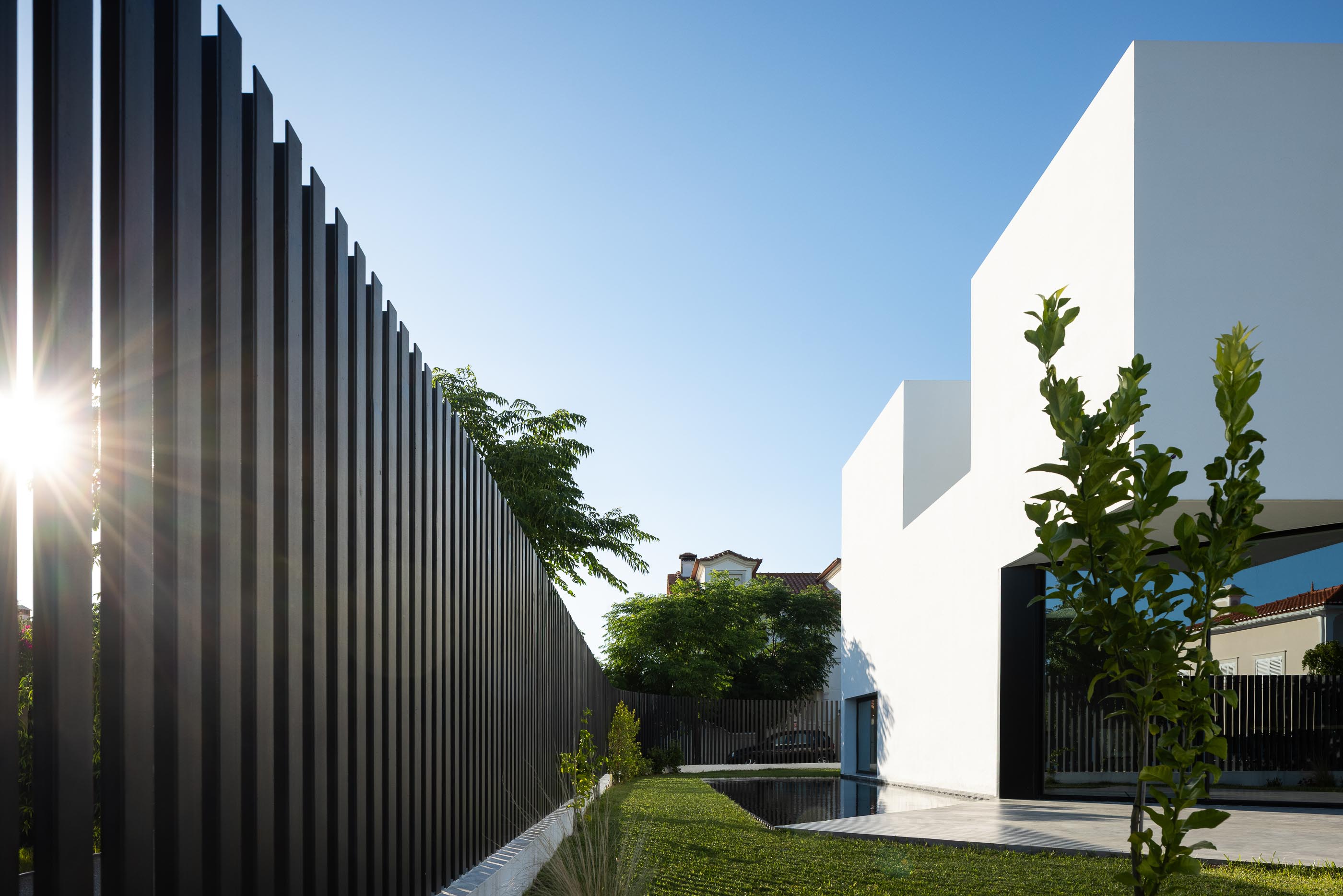 Exterior: Vedação preta vertical, relvado e fachada lateral da casa branca. — Casa DR arquitetura NMDARQ – Nuno Miguel Dias, Arquitecto em Torres Novas