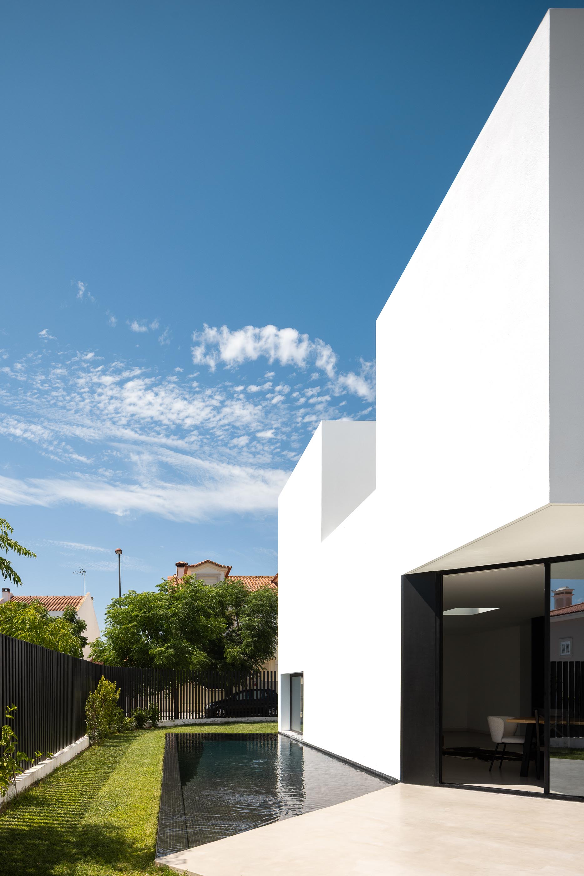 Exterior: Piscina retangular preta junto à casa branca com porta de correr preta. — Casa DR arquitetura NMDARQ – Nuno Miguel Dias, Arquitecto em Torres Novas