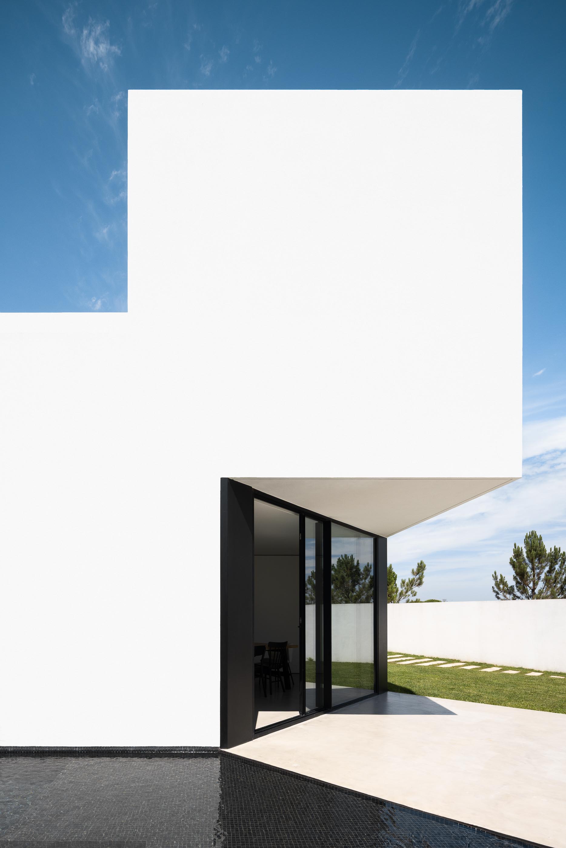 Exterior: Vista lateral da casa branca com piscina preta e porta de correr para o interior. — Casa DR arquitetura NMDARQ – Nuno Miguel Dias, Arquitecto em Torres Novas