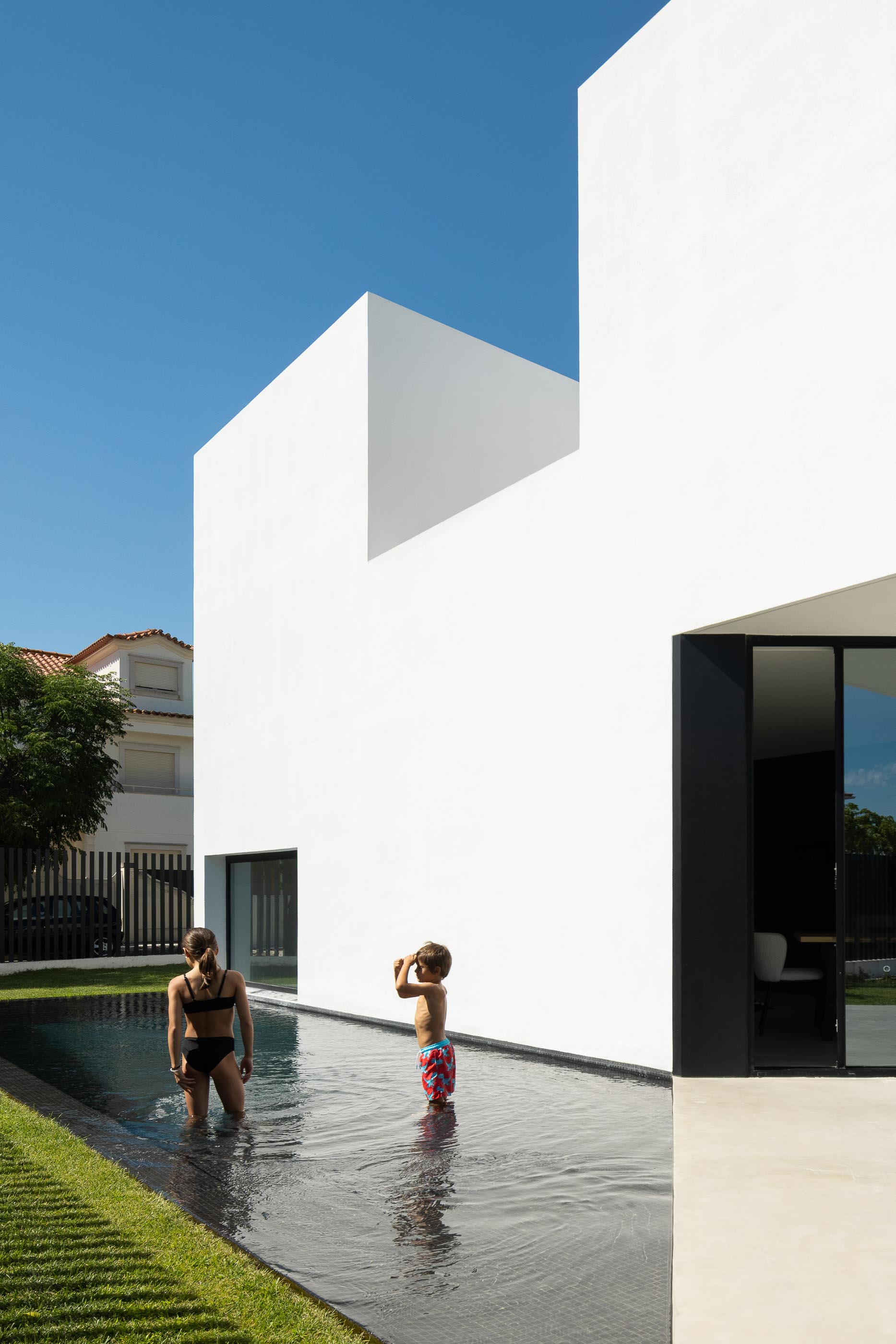 Exterior: Crianças na piscina preta junto à casa branca de linhas retas. — Casa DR arquitetura NMDARQ – Nuno Miguel Dias, Arquitecto em Torres Novas