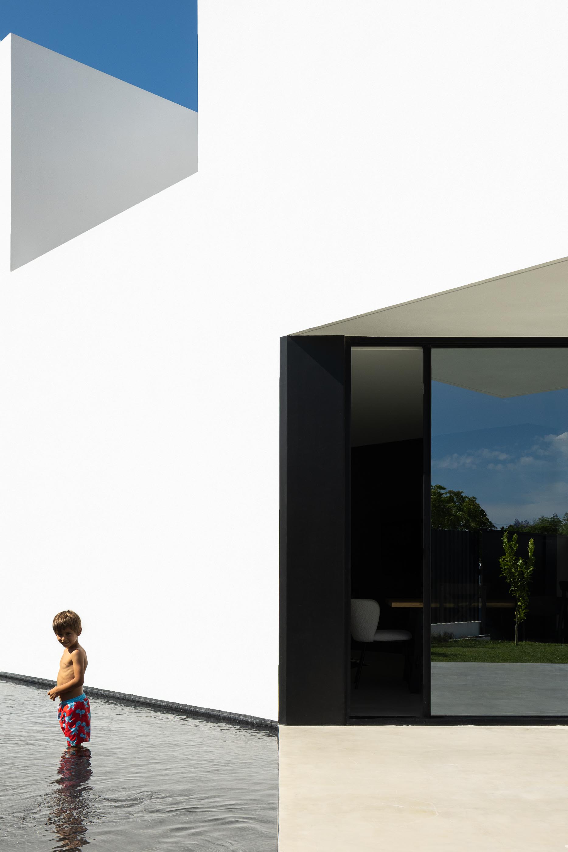 Exterior: Criança na piscina preta, com janela para o interior da casa branca. — Casa DR arquitetura NMDARQ – Nuno Miguel Dias, Arquitecto em Torres Novas