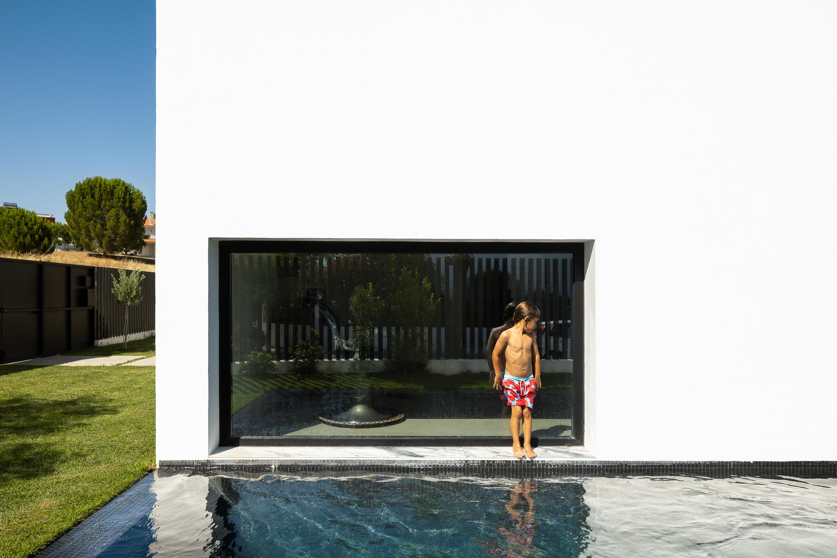Exterior: Crianças na piscina preta com vista para janela da casa branca. — Casa DR arquitetura NMDARQ – Nuno Miguel Dias, Arquitecto em Torres Novas