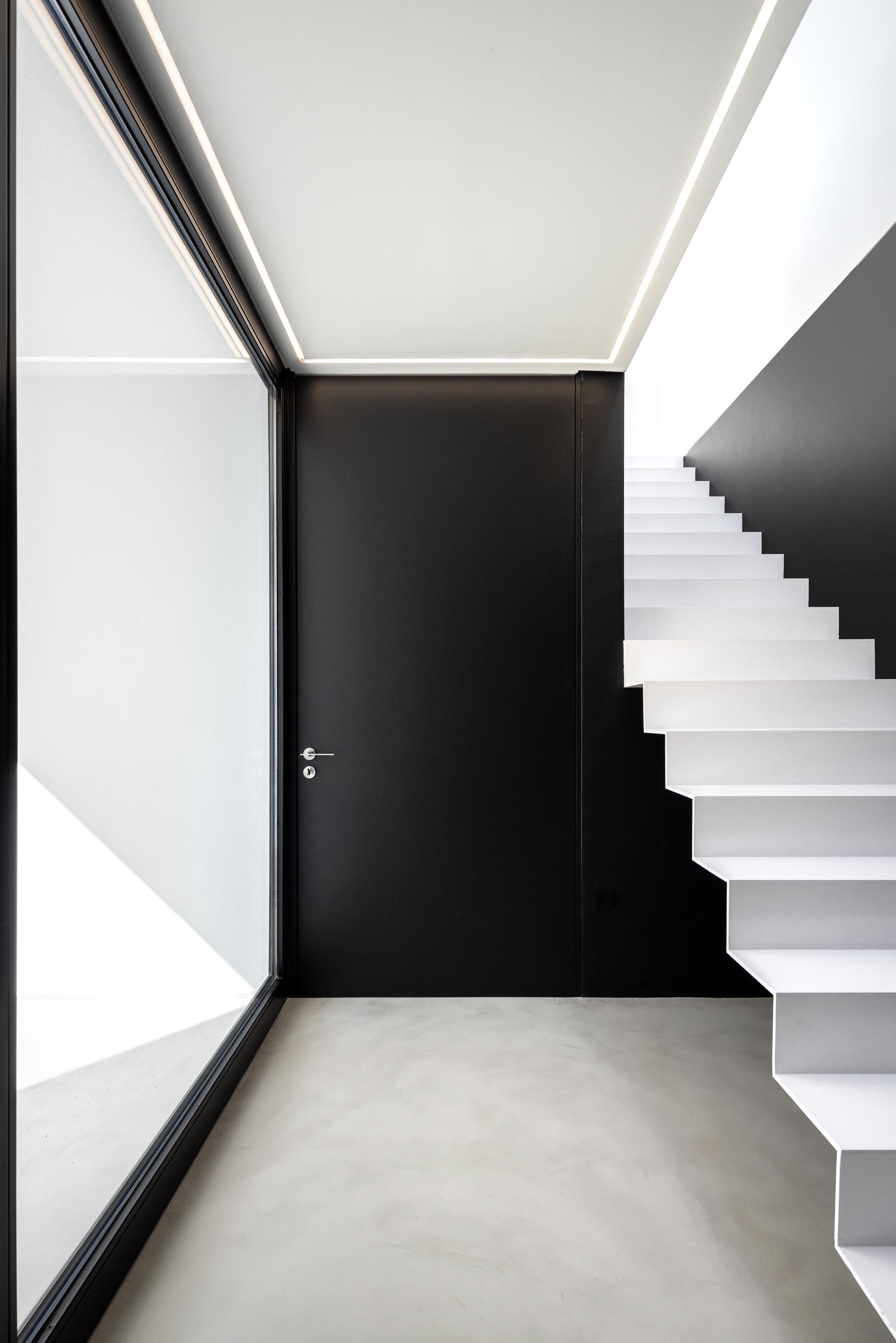 Corredor: Escadas, porta de correr preta e pavimento cinza com iluminação linear. — Casa DR arquitetura NMDARQ – Nuno Miguel Dias, Arquitecto em Torres Novas