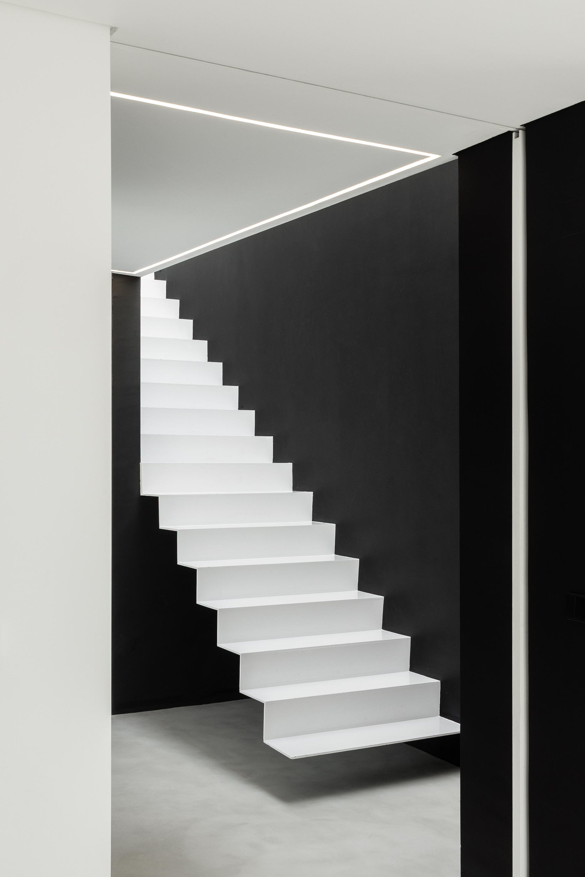 Escadas: Homem a subir escadas brancas com paredes pretas e claraboia. — Casa DR arquitetura NMDARQ – Nuno Miguel Dias, Arquitecto em Torres Novas