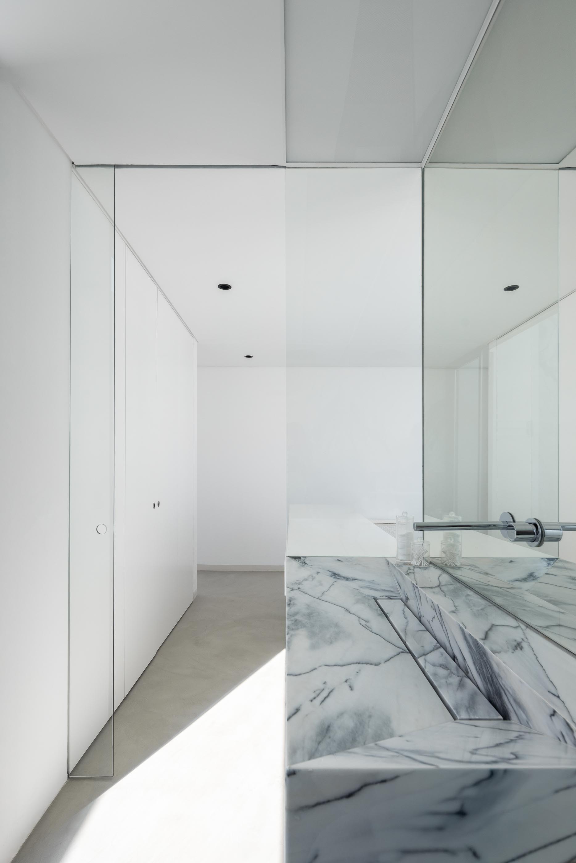 Quarto: Cama branca, armários brancos e casa de banho com mármore ao fundo. — Casa DR arquitetura NMDARQ – Nuno Miguel Dias, Arquitecto em Torres Novas