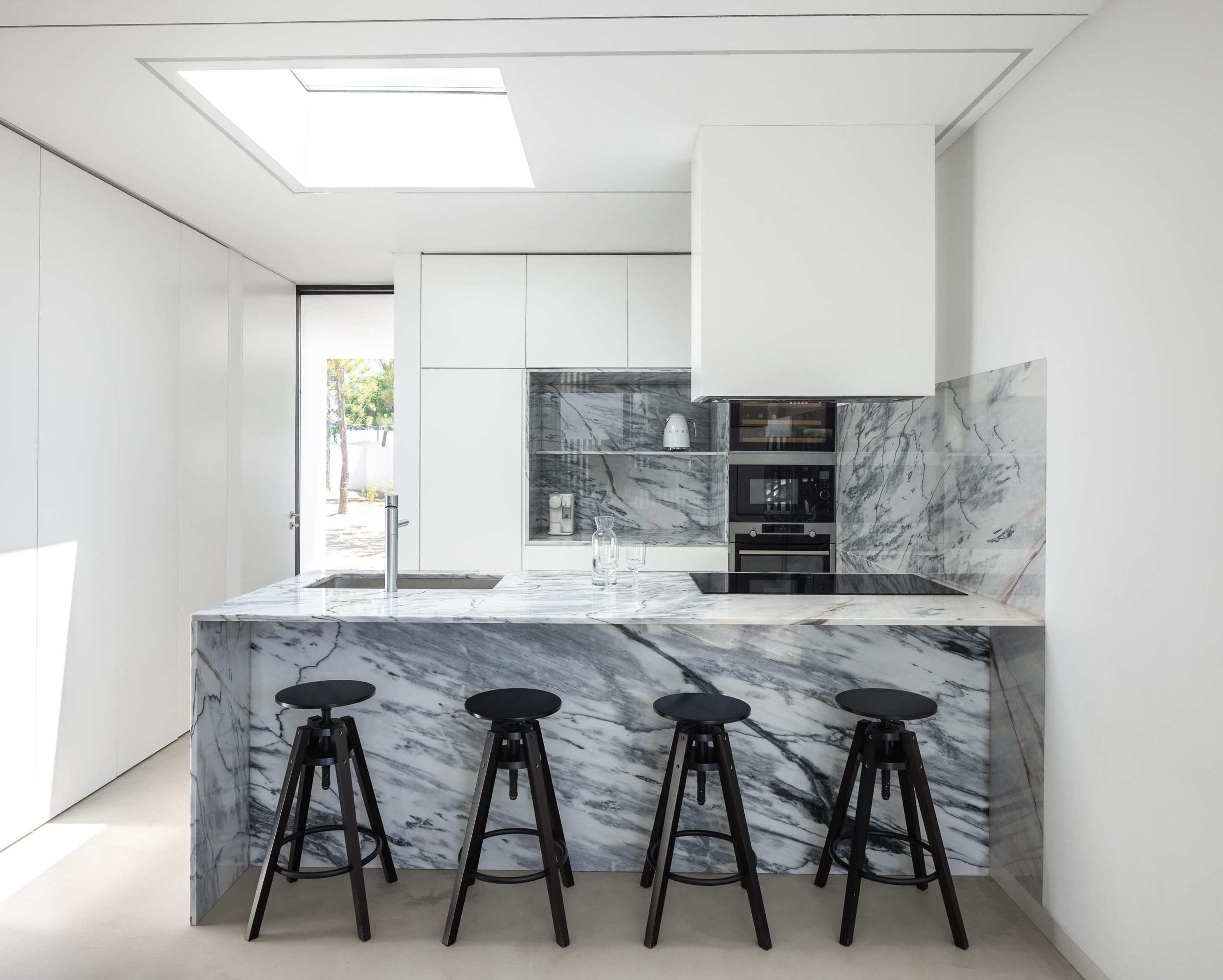 Cozinha: Ilha em mármore, mesa de madeira e sala de estar com sofá castanho. — Casa DR arquitetura NMDARQ – Nuno Miguel Dias, Arquitecto em Torres Novas