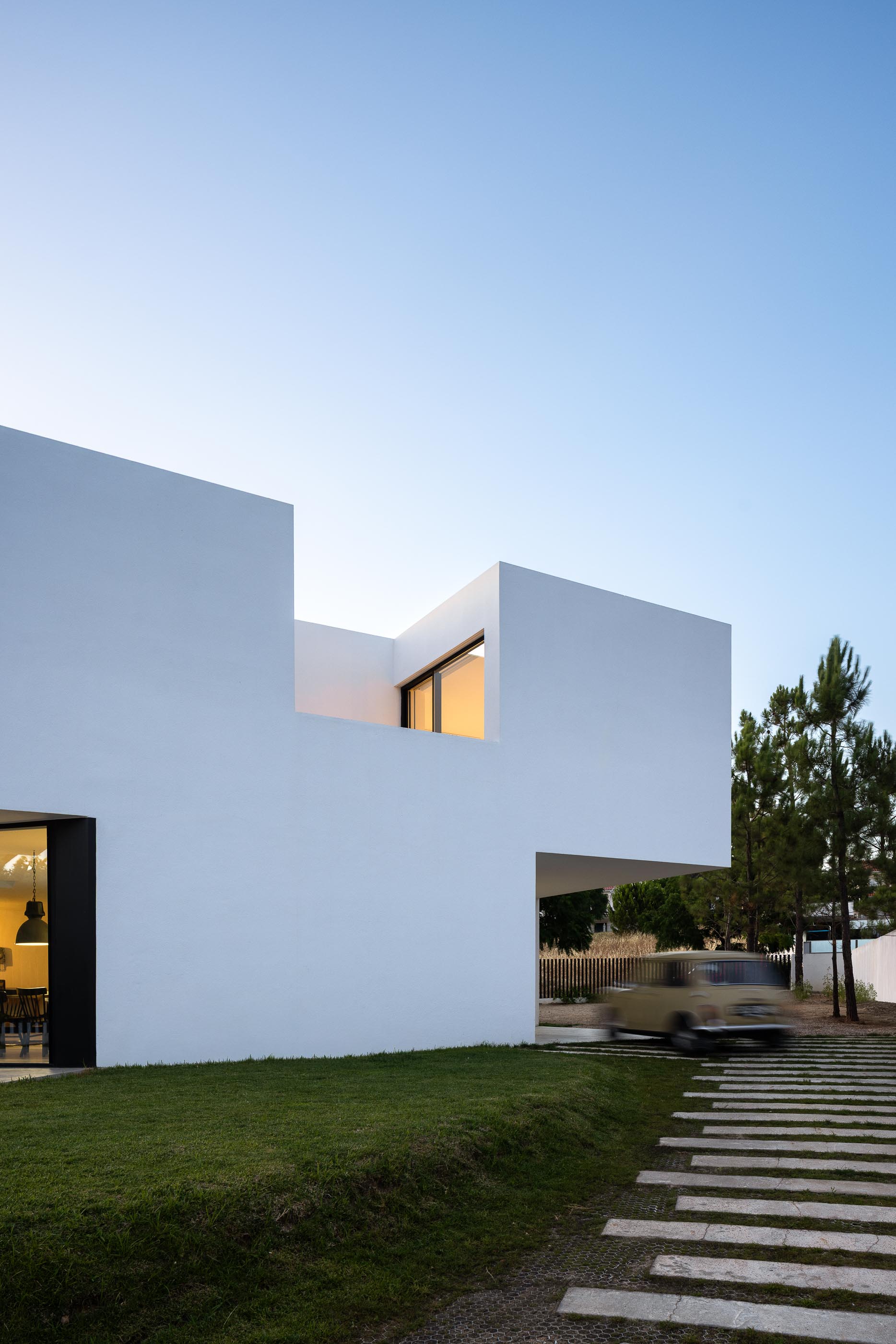 Exterior: Casa branca minimalista com pessoa na varanda ao entardecer. — Casa DR arquitetura NMDARQ – Nuno Miguel Dias, Arquitecto em Torres Novas