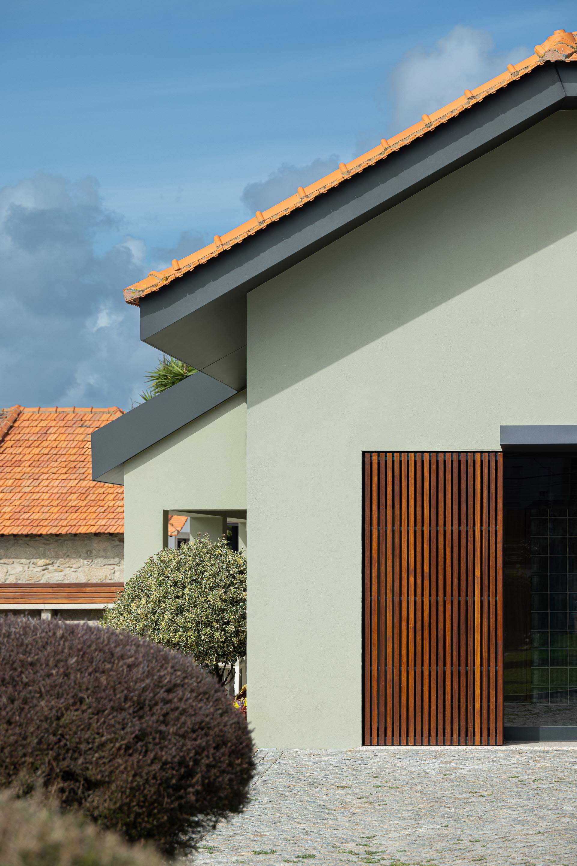 Exterior: Fachada da casa com revestimento verde claro, telhado de telha, porta em ripas de madeira e janelas com caixilharia cinzenta. — Casa do Engenho arquitetura silverline em Vila Nova de Gaia