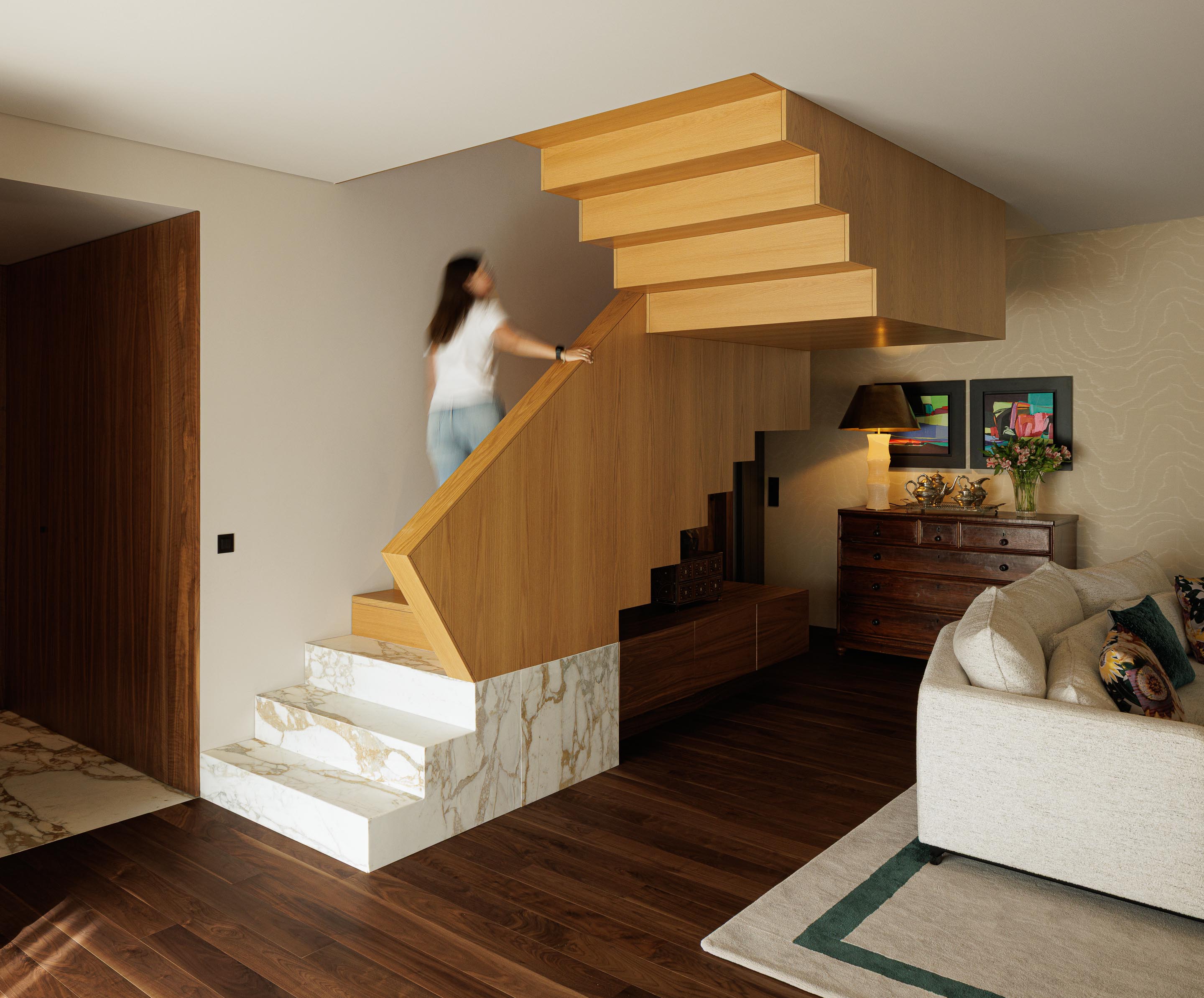 Sala de estar: Escadas em madeira e mármore, sofá branco com almofadas coloridas, alcatifa geométrica e pavimento em madeira escura. — Casa do Engenho arquitetura silverline em Vila Nova de Gaia