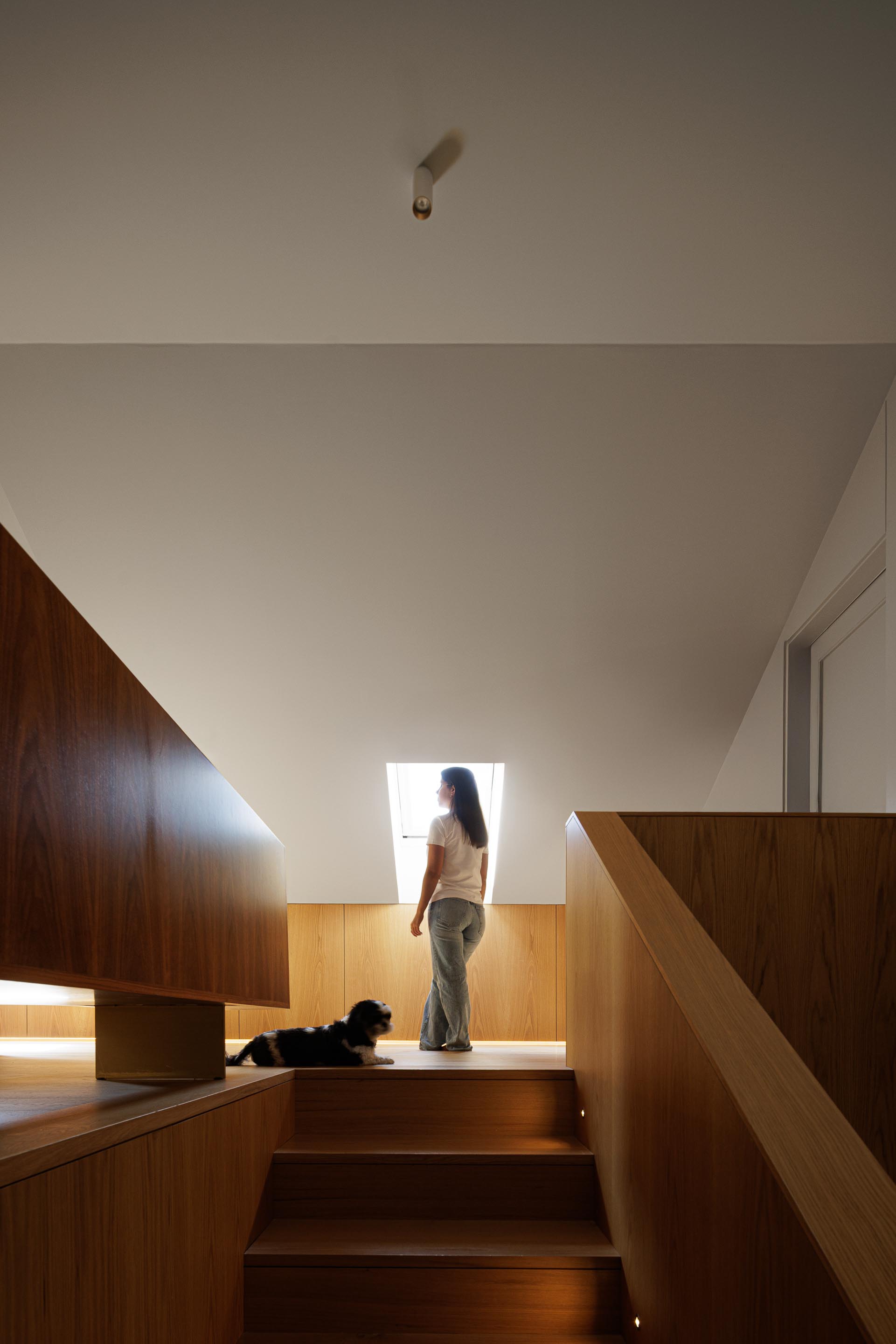 Corredor: Escadas em madeira clara, com candeeiro embutido no teto e parede revestida em madeira escura. — Casa do Engenho arquitetura silverline em Vila Nova de Gaia