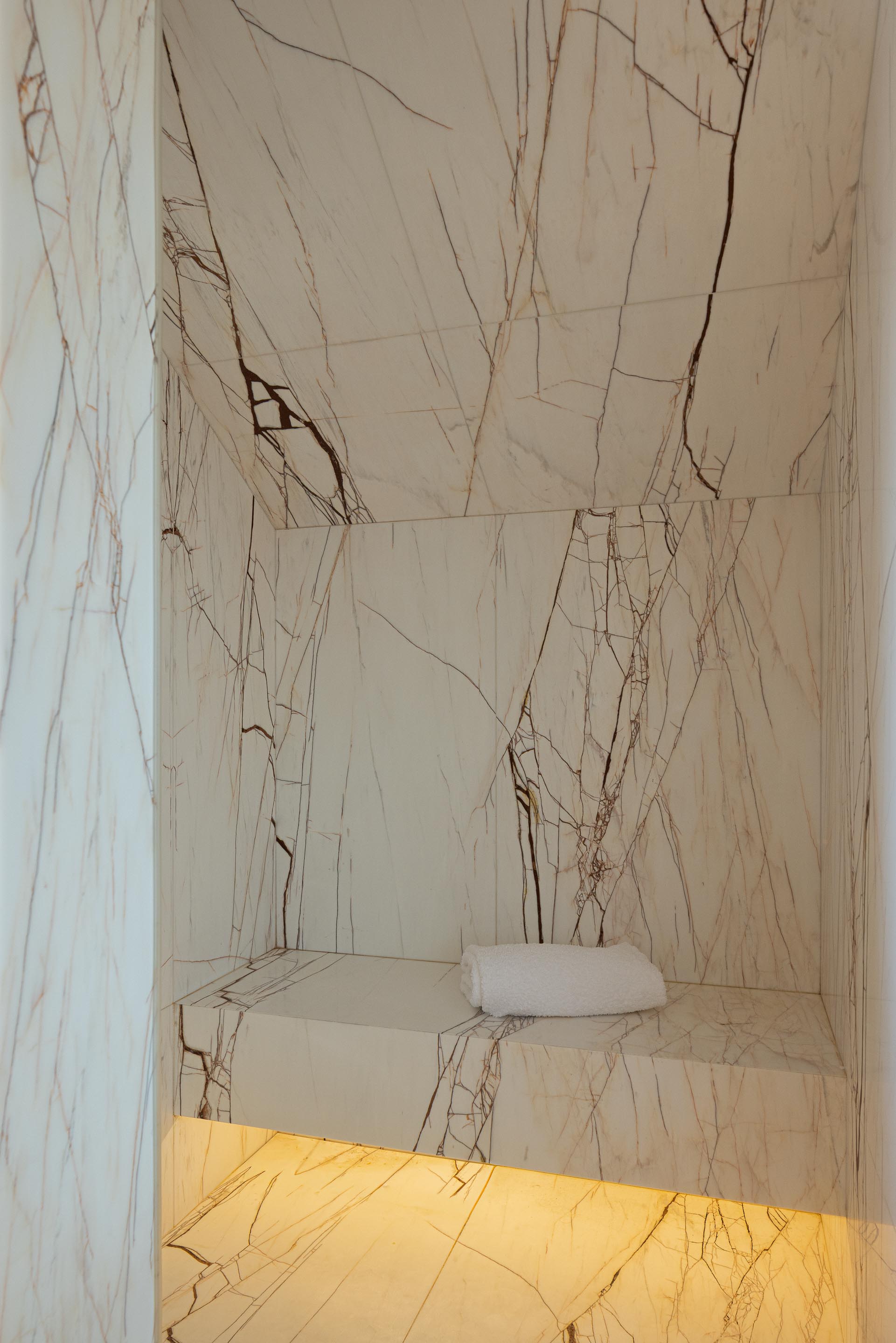 Casa de banho: Interior da cabine de duche com revestimento em mármore branco e banco iluminado. — Casa do Engenho arquitetura silverline em Vila Nova de Gaia