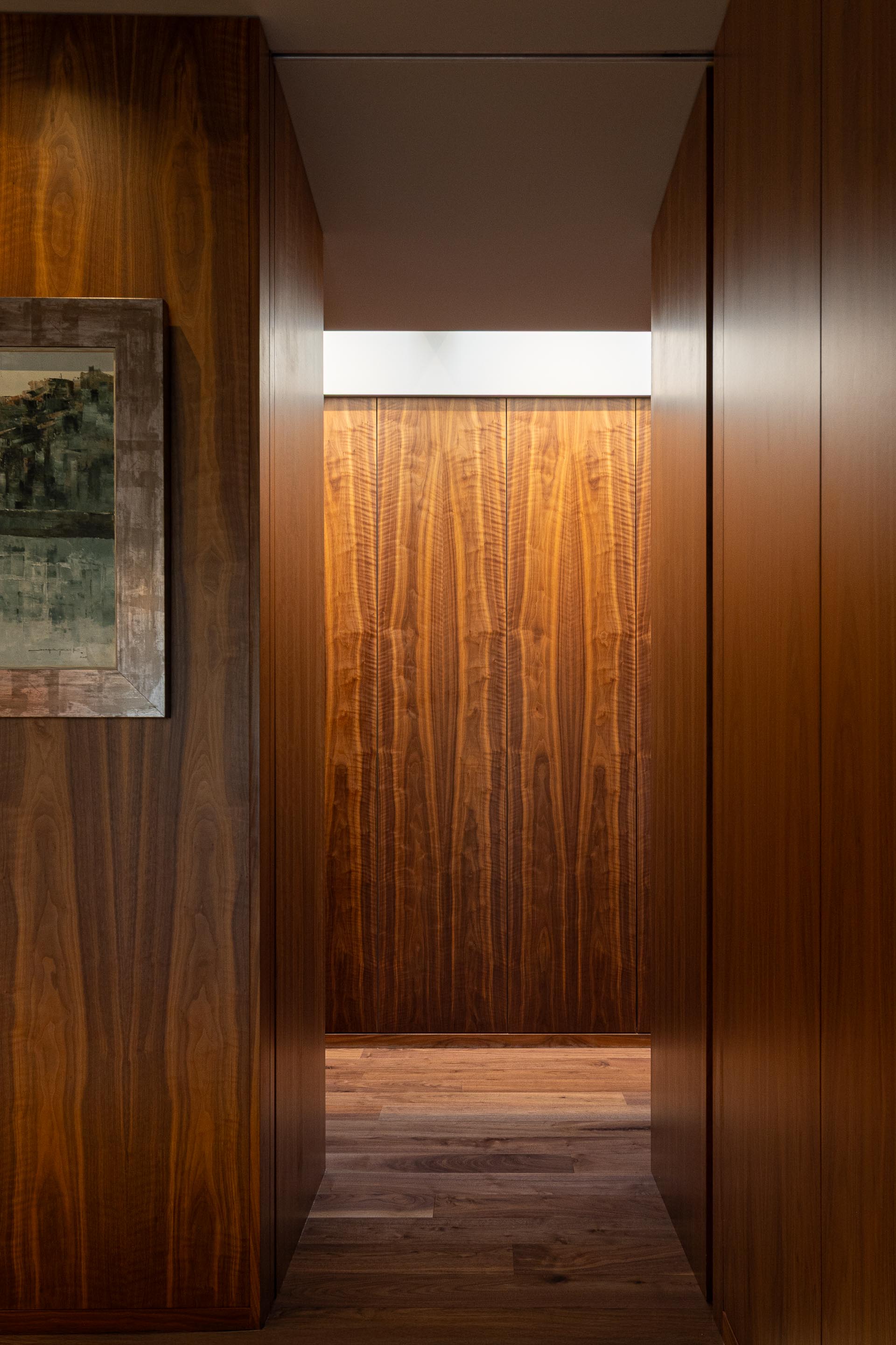 Corredor: Detalhe da parede revestida em madeira escura, com um quadro e uma porta ao fundo. — Casa do Engenho arquitetura silverline em Vila Nova de Gaia