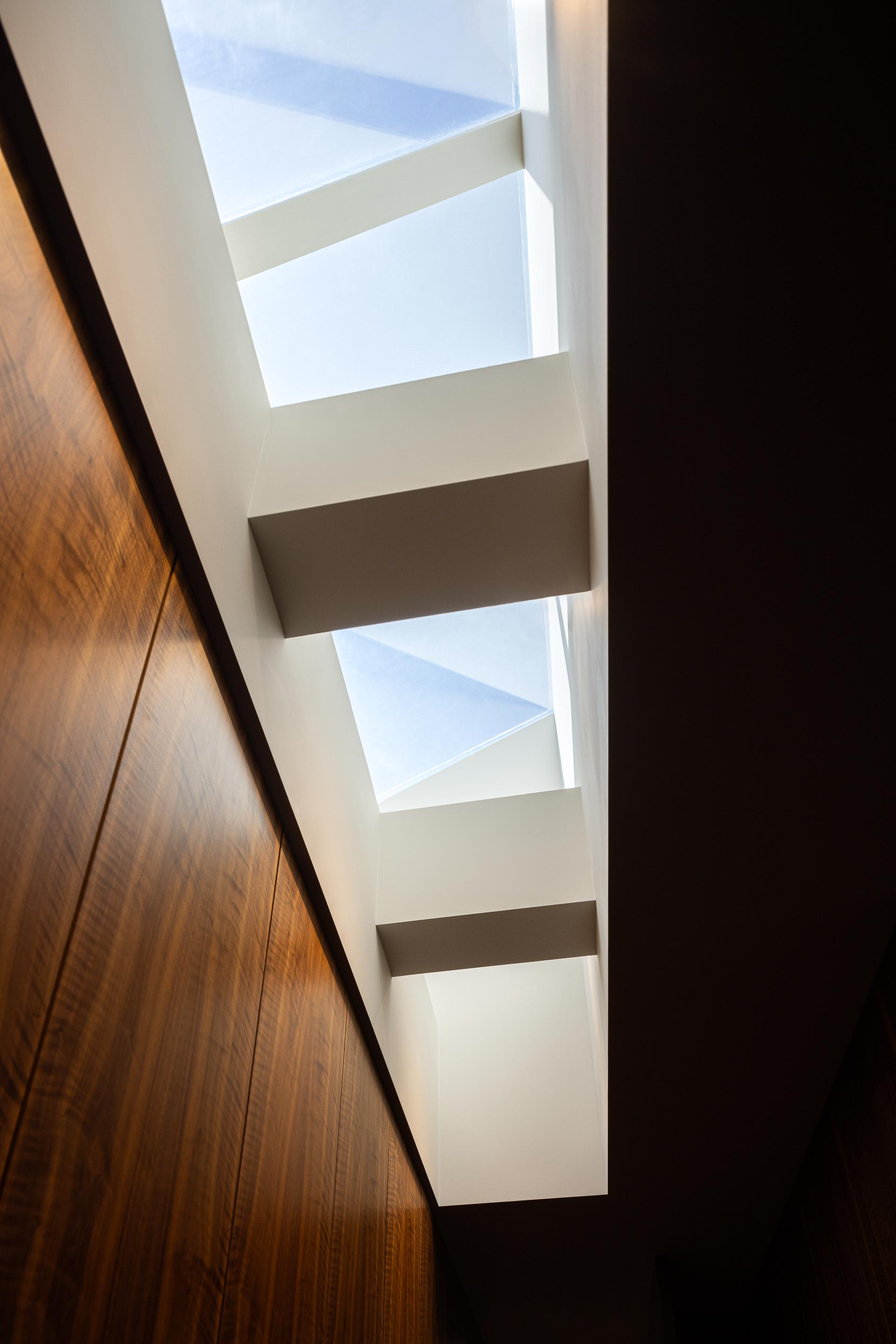 Corredor: Detalhe da claraboia no teto, com estrutura em branco e paredes revestidas em madeira escura. — Casa do Engenho arquitetura silverline em Vila Nova de Gaia