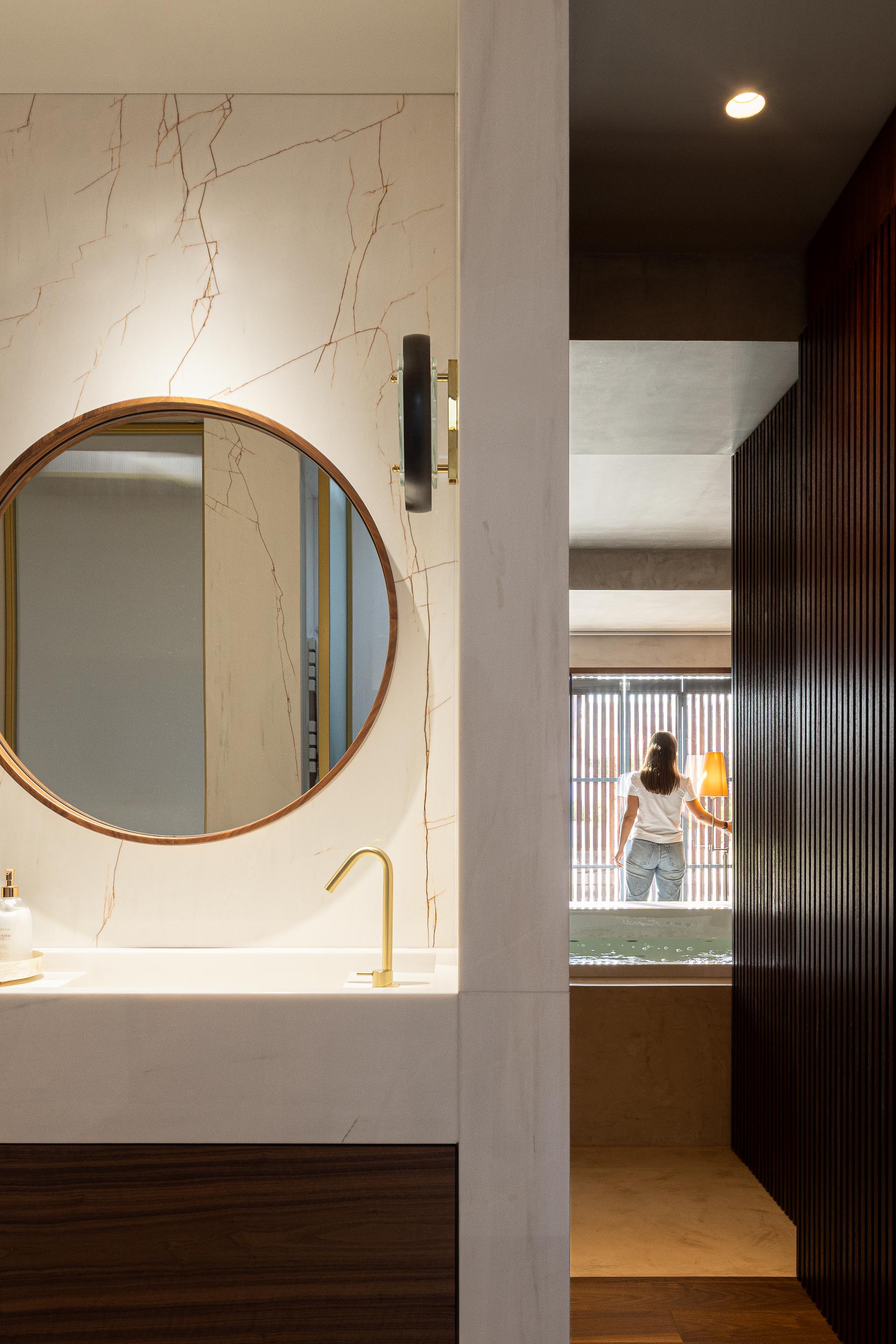 Casa de banho: Lavatório branco com torneira dourada, espelho redondo e parede revestida em mármore. — Casa do Engenho arquitetura silverline em Vila Nova de Gaia