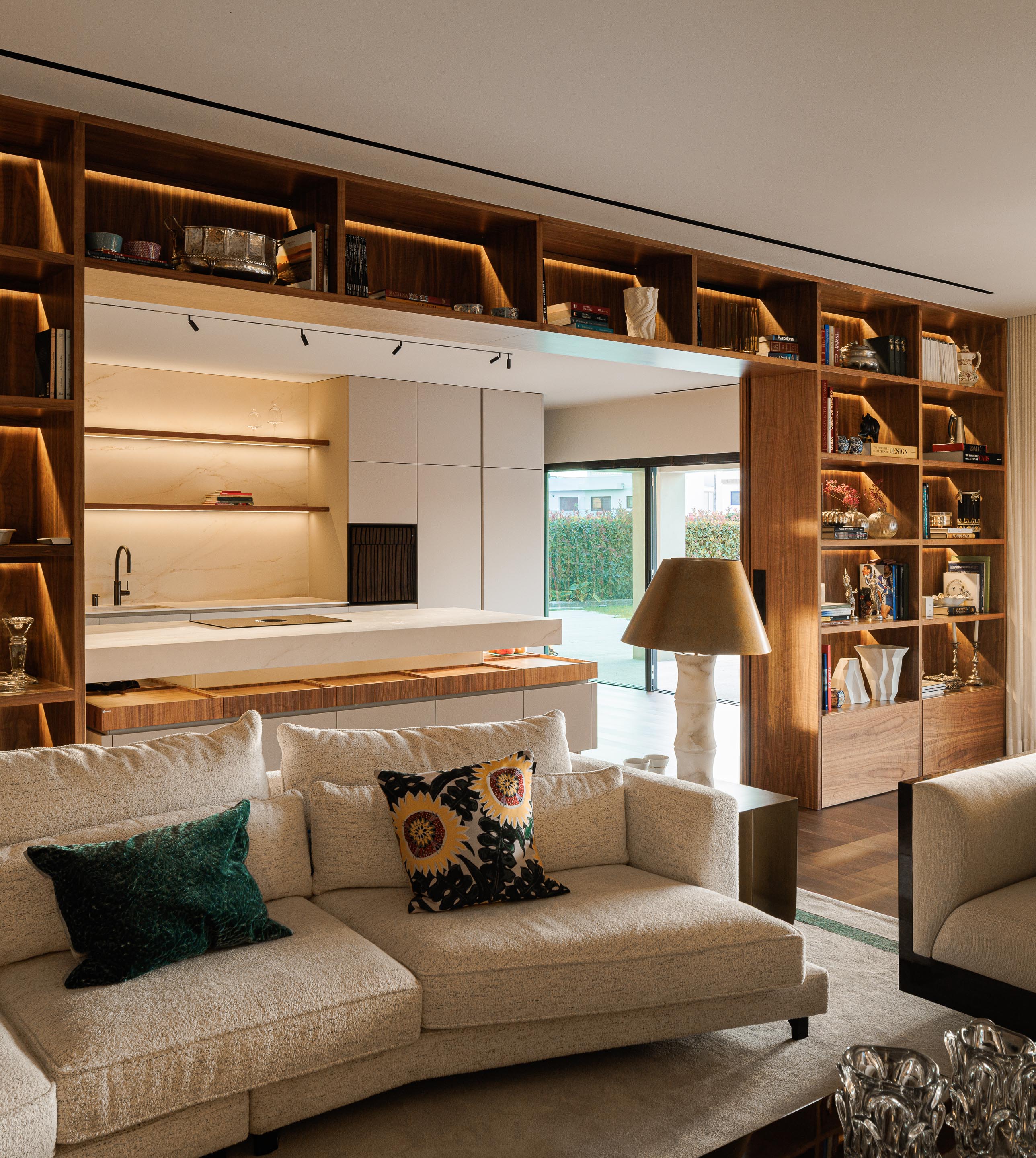 Sala de estar: Estantes em madeira escura, cozinha com bancada em mármore branco e sofá branco com almofadas coloridas. — Casa do Engenho arquitetura silverline em Vila Nova de Gaia