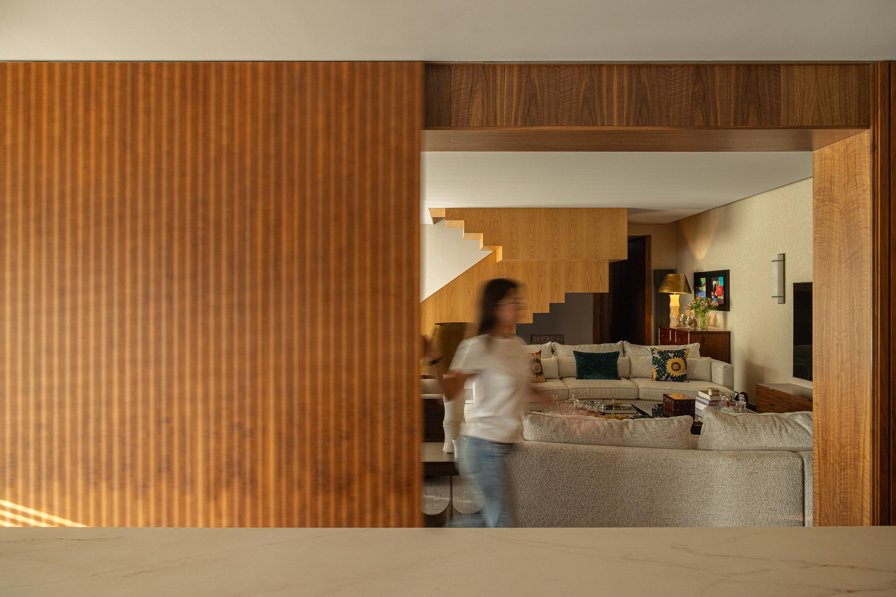 Sala de estar: Vista da sala de estar a partir da cozinha, com porta de correr em ripas de madeira escura. — Casa do Engenho arquitetura silverline em Vila Nova de Gaia