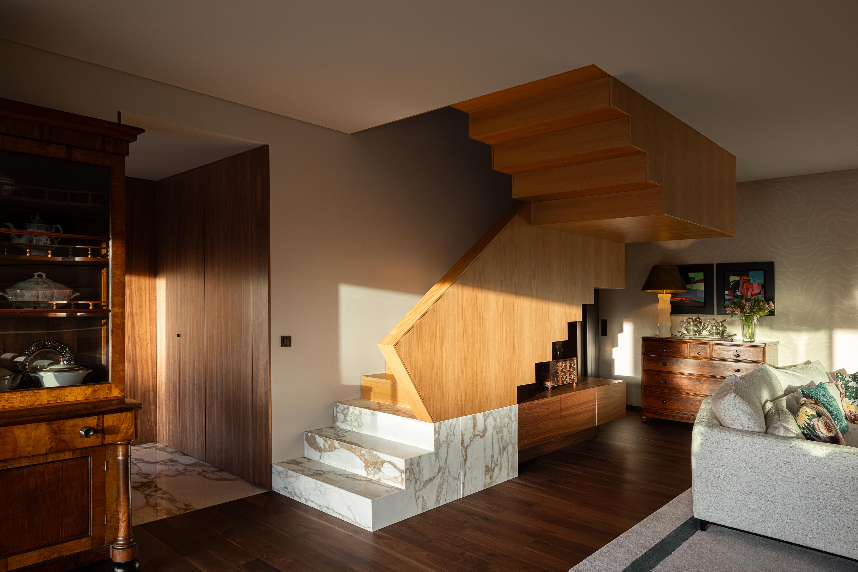 Sala de estar: Escadas em madeira e mármore, estantes em madeira escura e mobiliário clássico. — Casa do Engenho arquitetura silverline em Vila Nova de Gaia